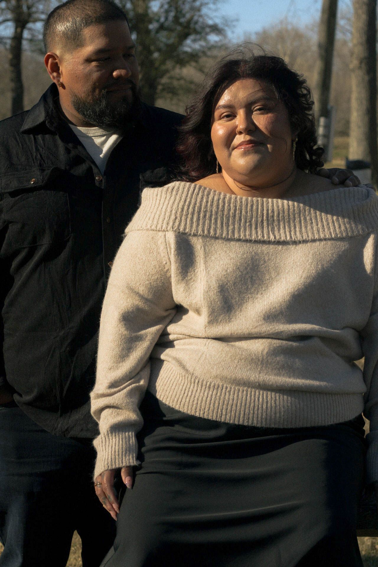 Two people share a joyful moment while posing outdoors near trees.
