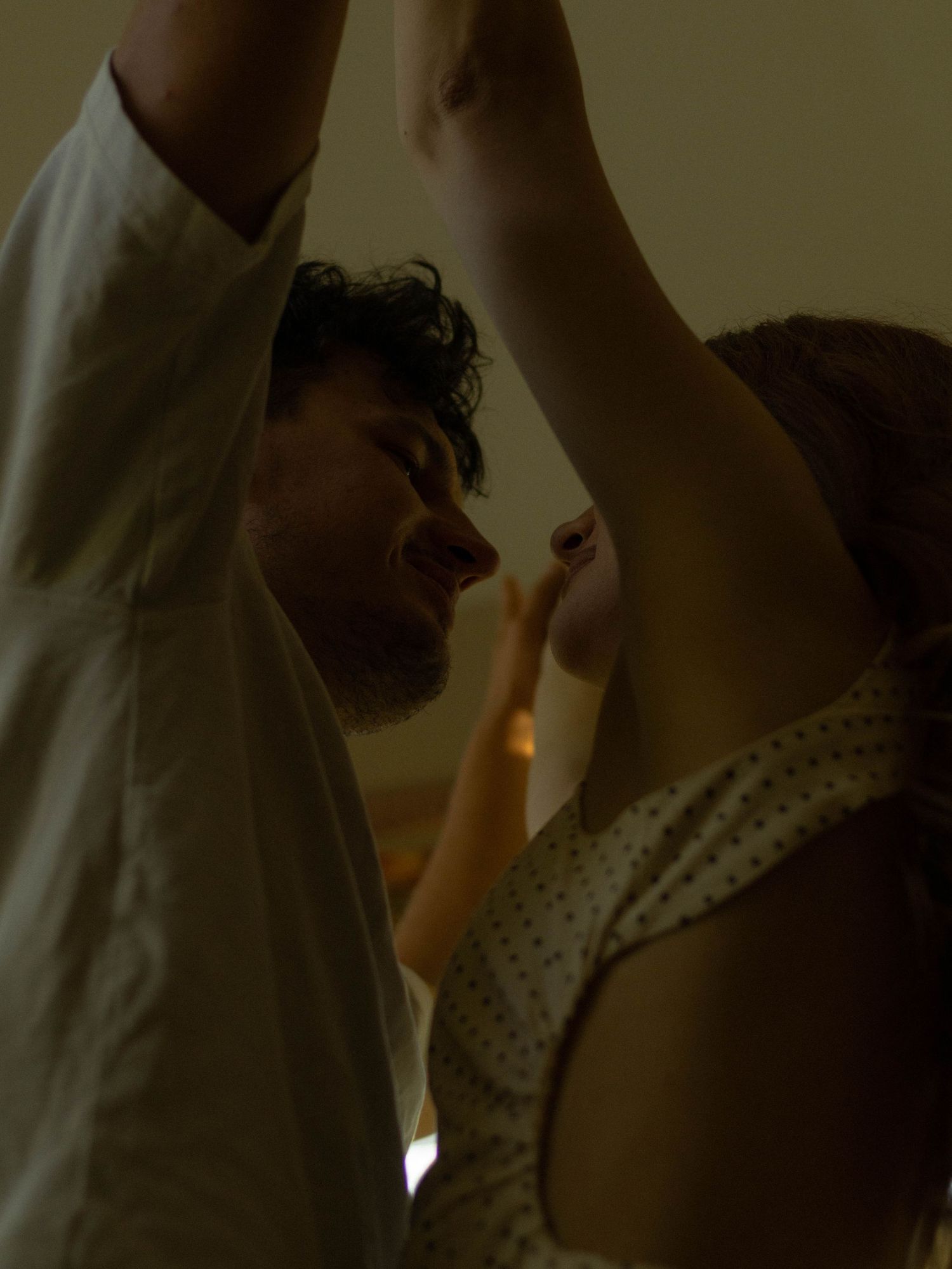 A man and woman dancing together intimately, arms raised, in warm dim lighting.