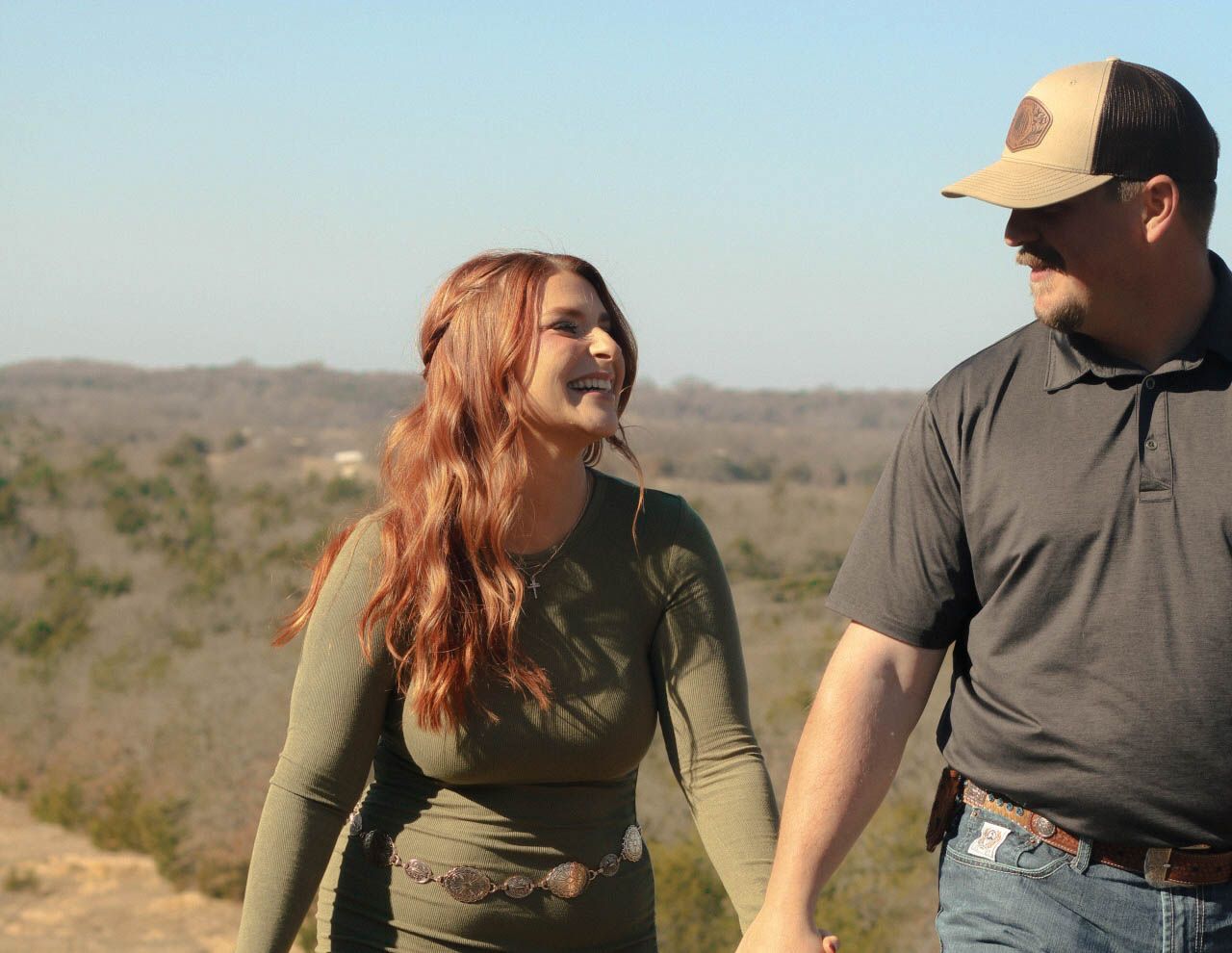 Couple walking together in a desert landscape with brown hills in the background.