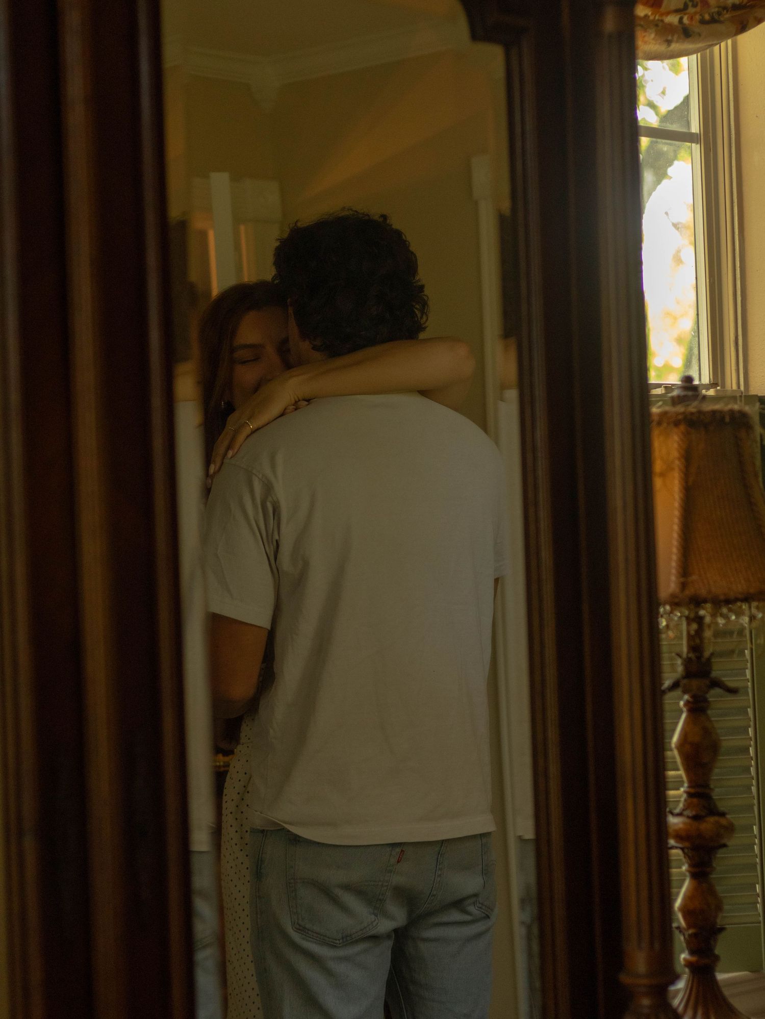 Couple embracing tenderly in a vintage bedroom reflected in an ornate full-length mirror.