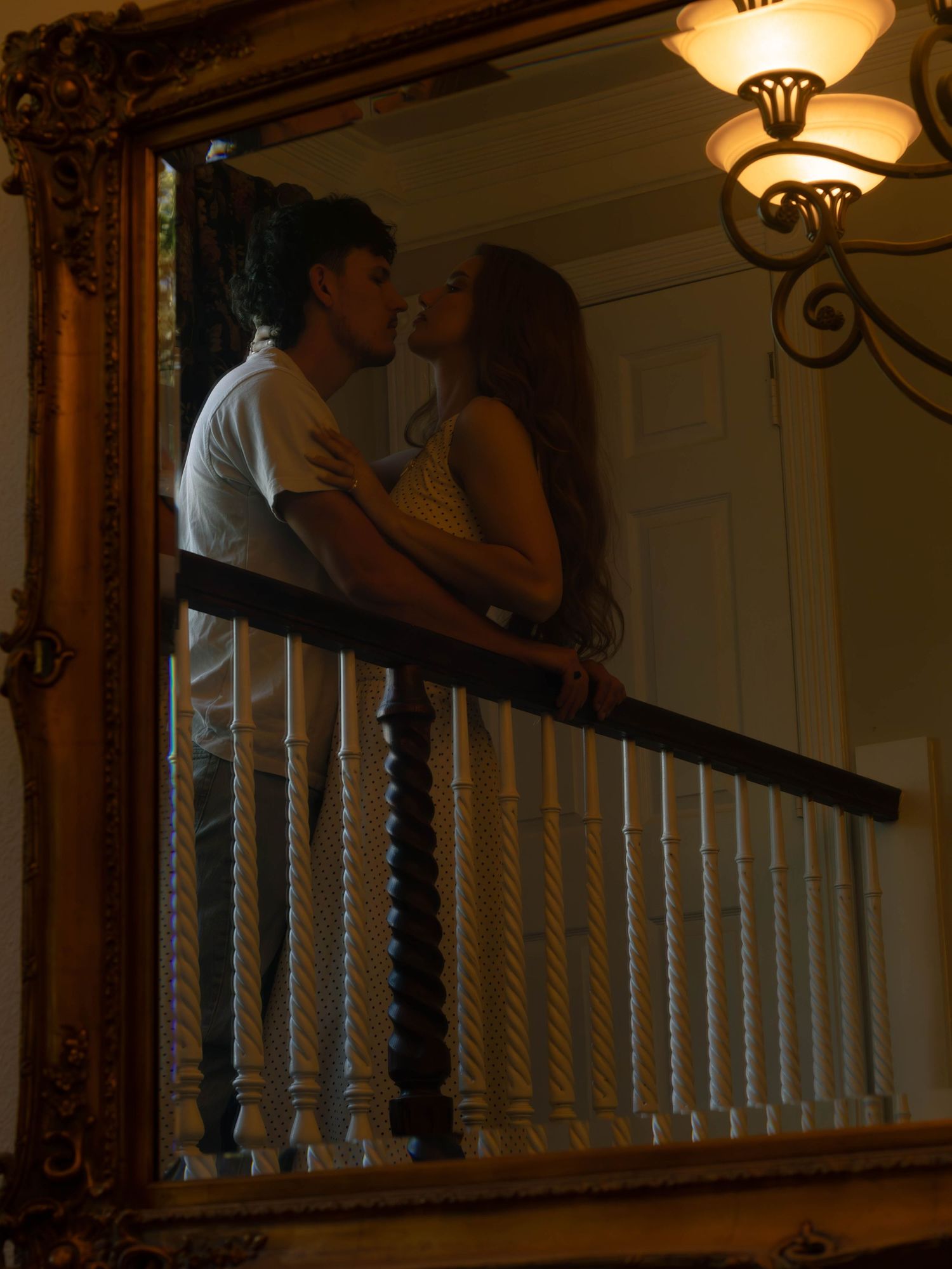 Couple sharing a romantic kiss on an elegant staircase balcony with white spindles and warm lighting.