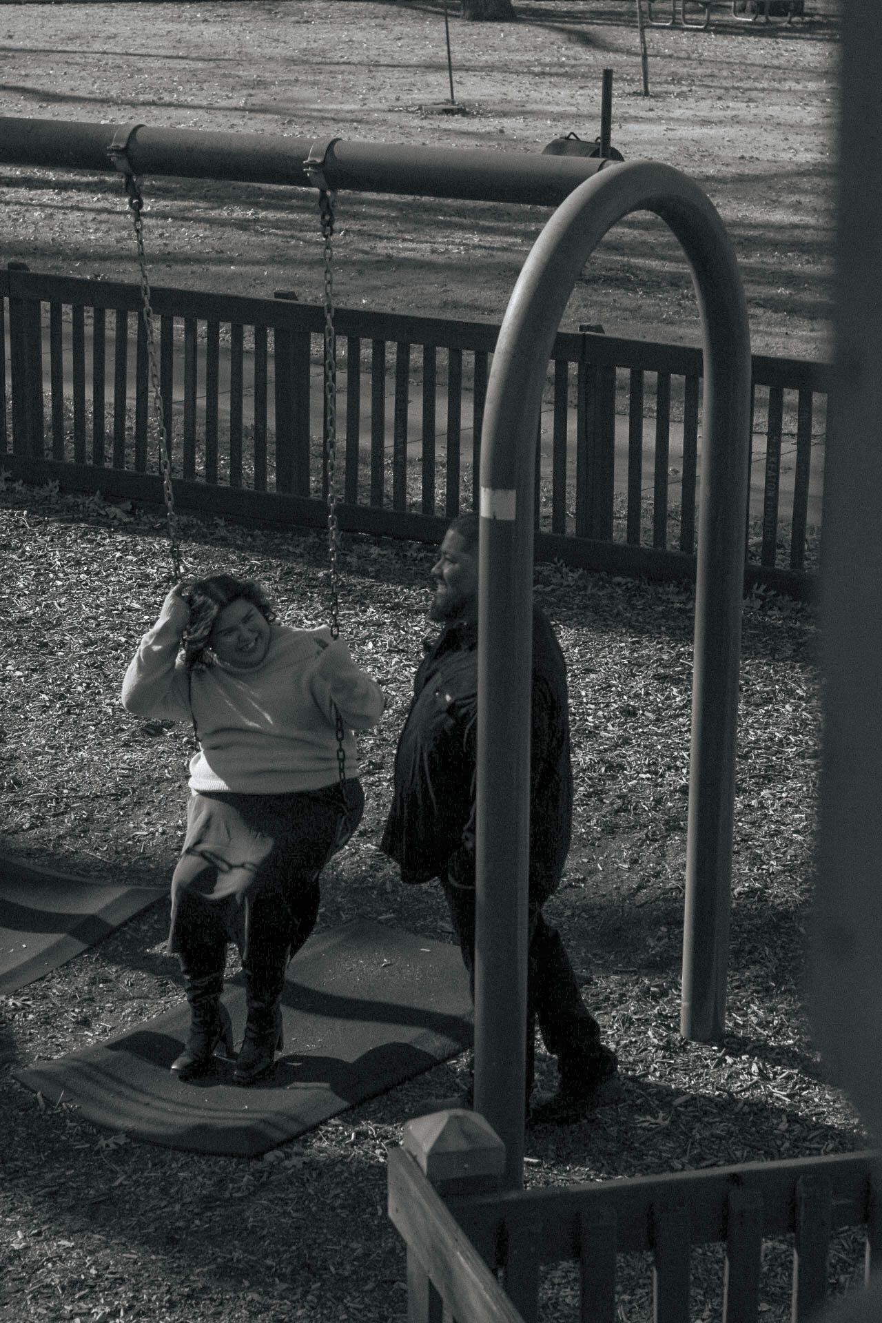 Two people relaxing on playground swings in a park setting.