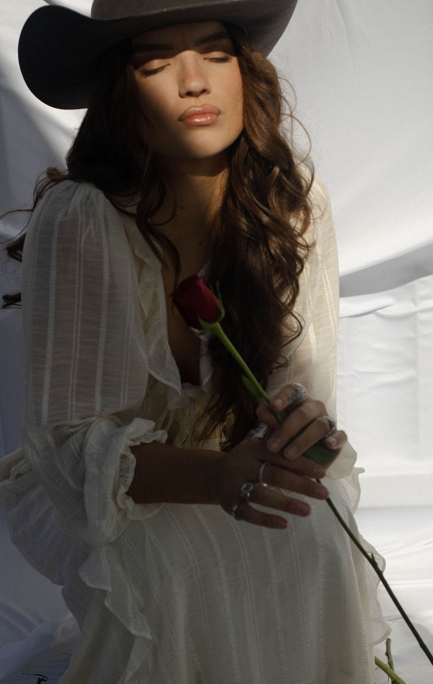 Artistic portrait series showing figure in white dress holding single rose against bright backlit window.