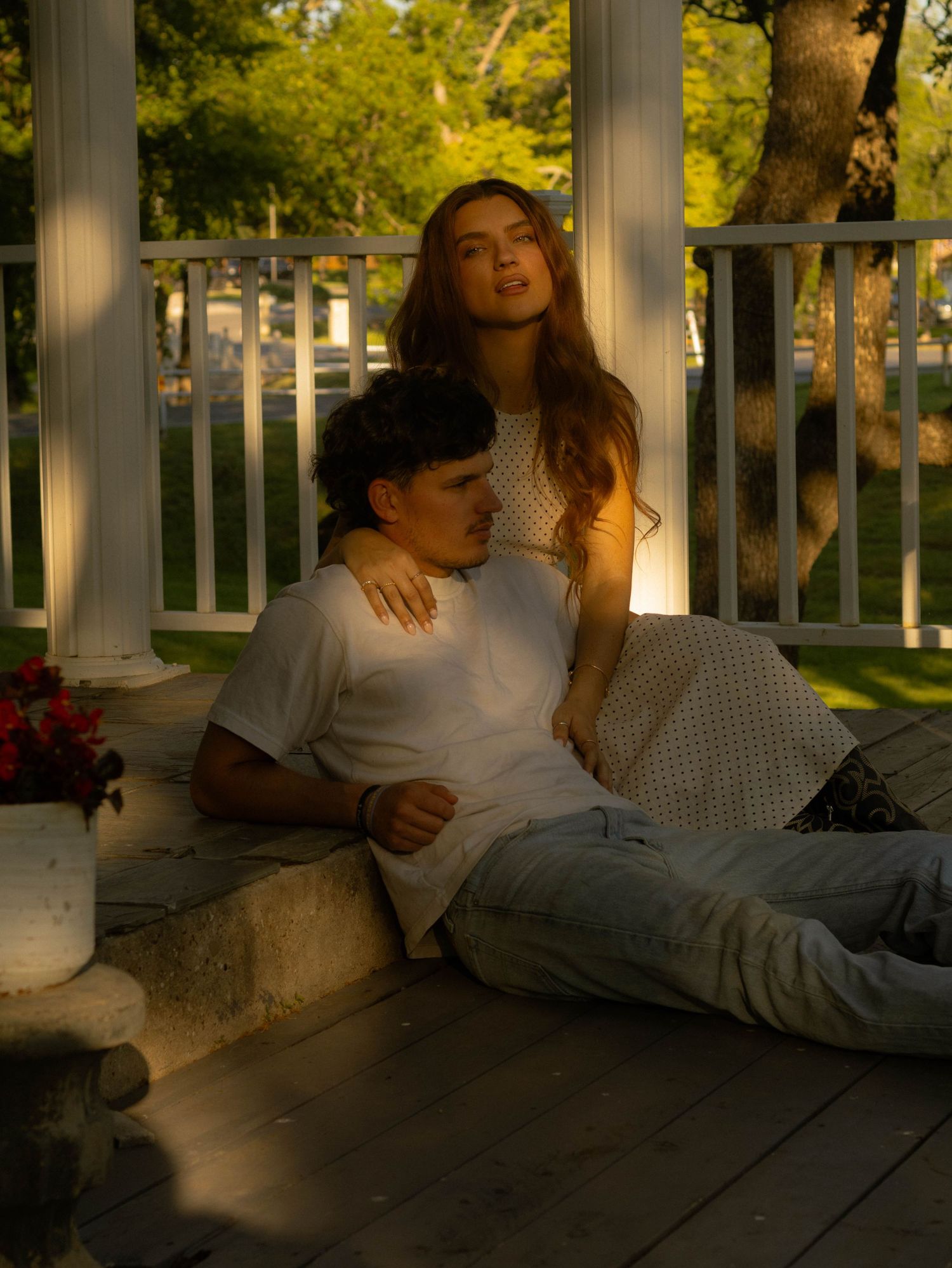 A young couple relaxes on a sunlit porch, the woman sitting above the man leaning against her.
