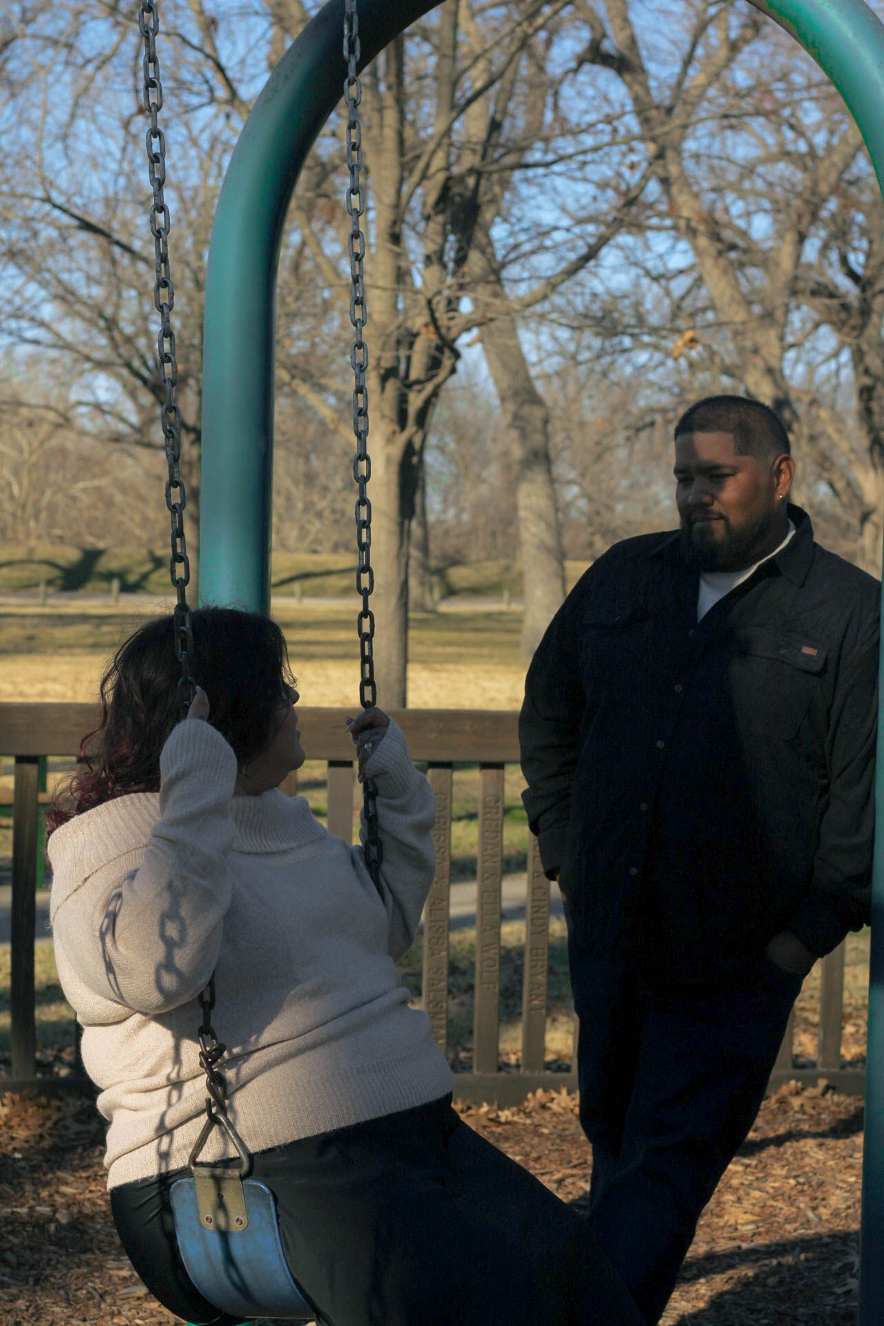 Two people spending time together at a park playground with metal swing set.
