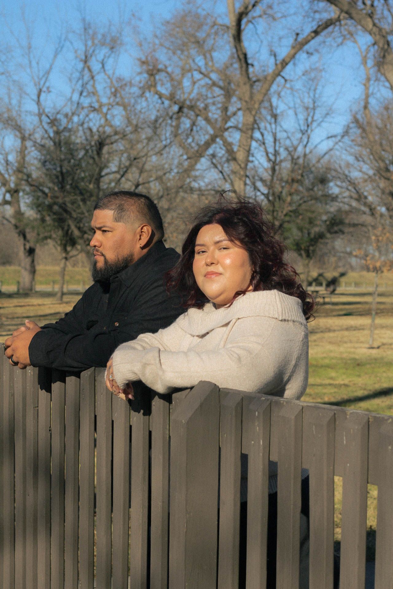 Two people rest their arms on a wooden fence while enjoying a peaceful moment outdoors.
