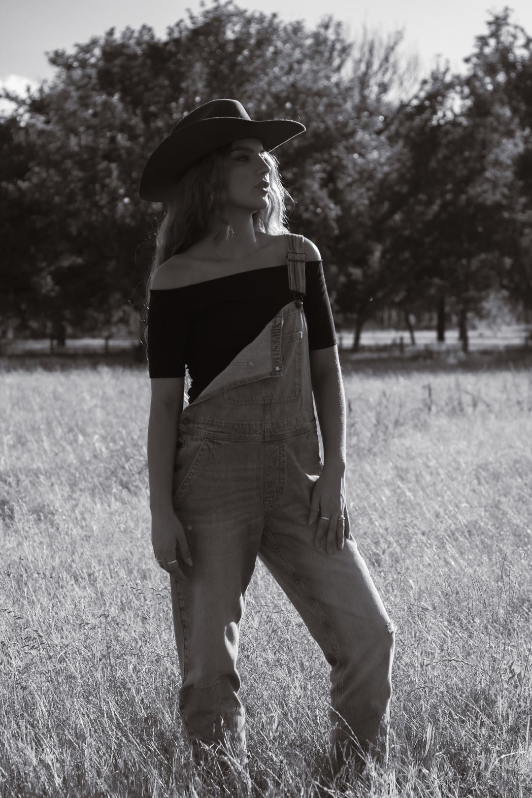 A silhouetted figure wearing overalls and a hat stands in a tall grass field.