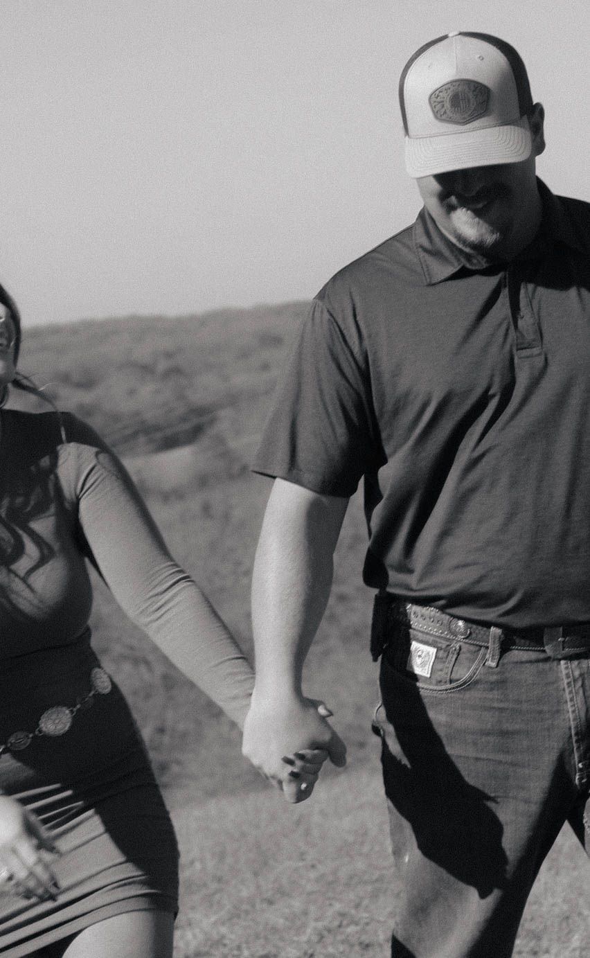 A couple holding hands in black and white photography against a rural backdrop.