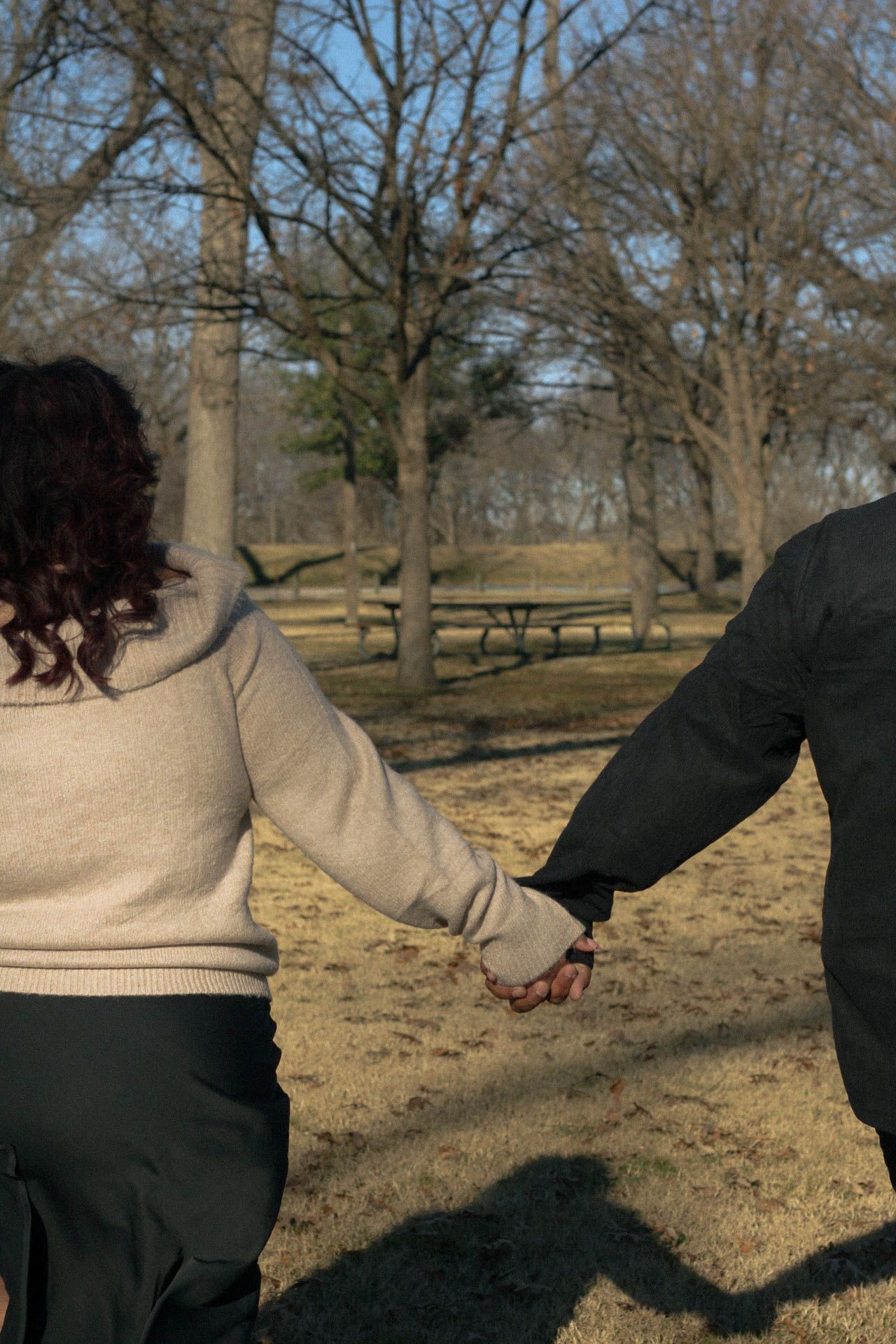 A couple walking through a park holding hands on a winter afternoon.