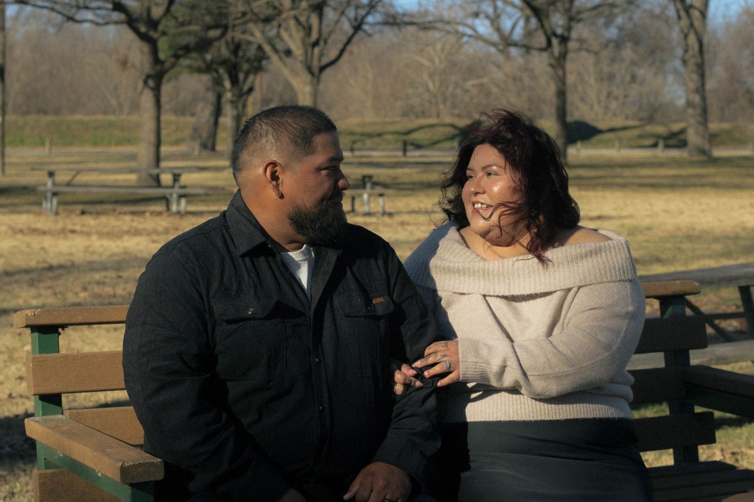 A couple sits together on a park bench having an intimate conversation.