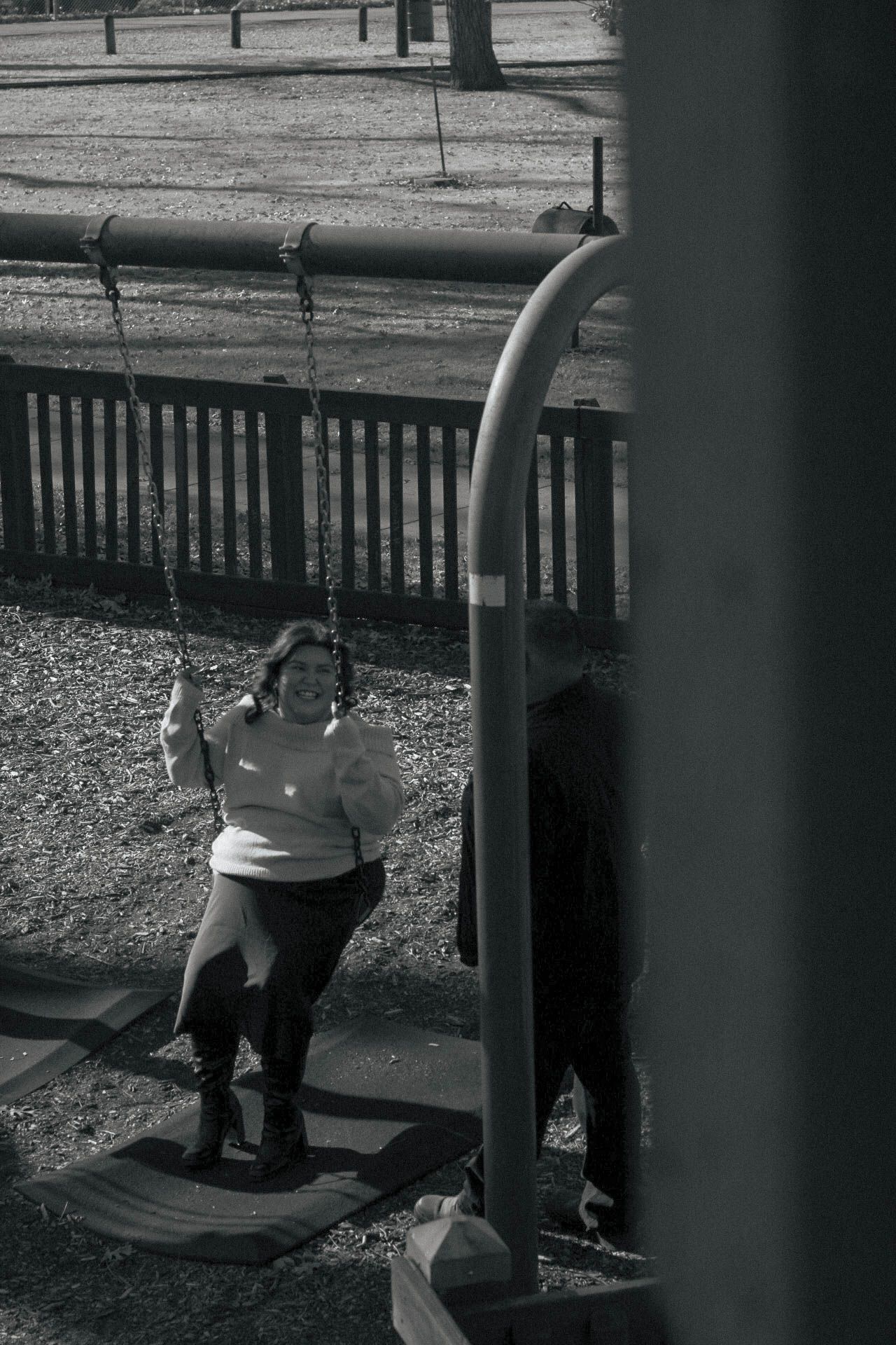 Two people enjoying swings at a public park on a winter day.