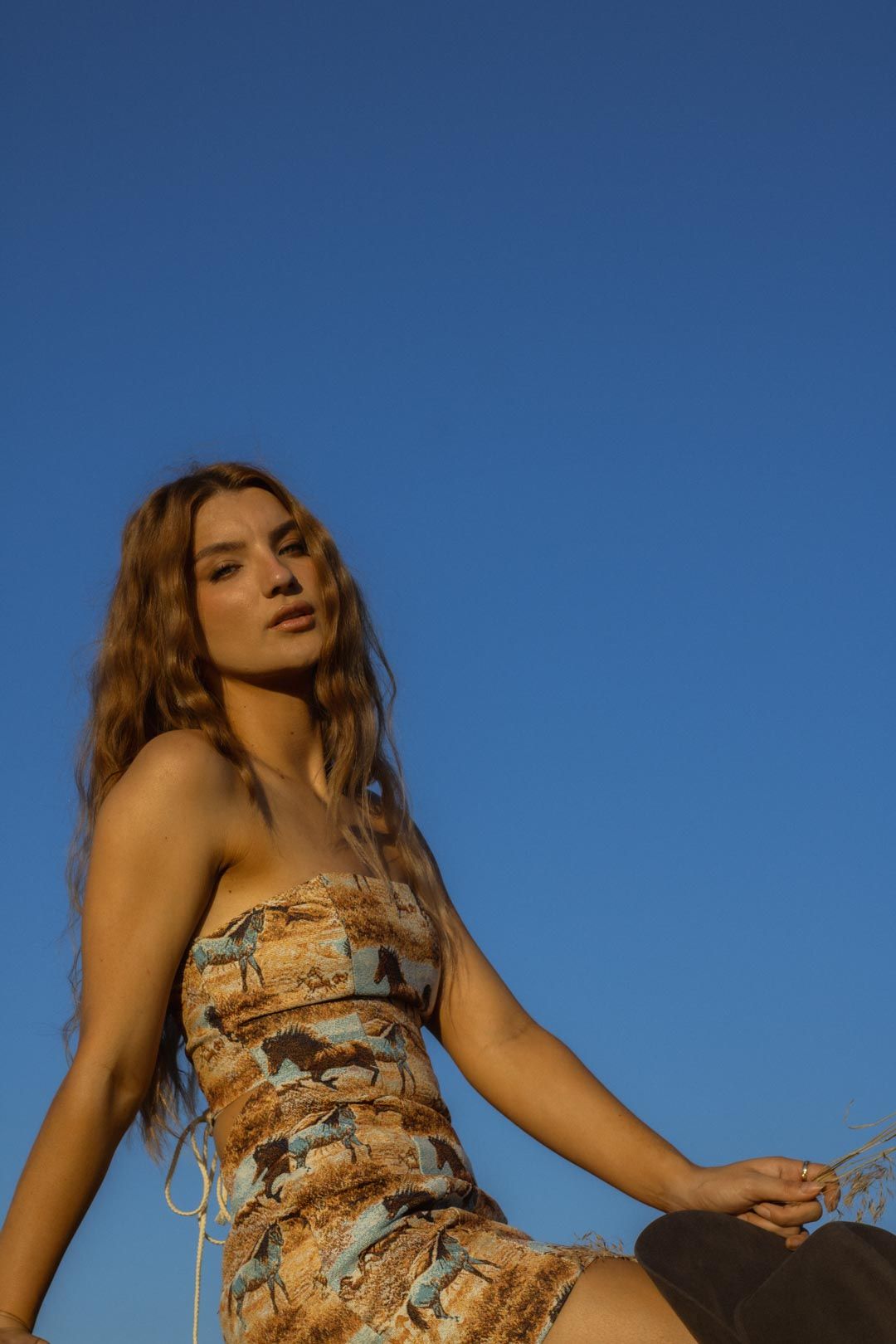 A person in a floral dress poses against a bright blue summer sky.