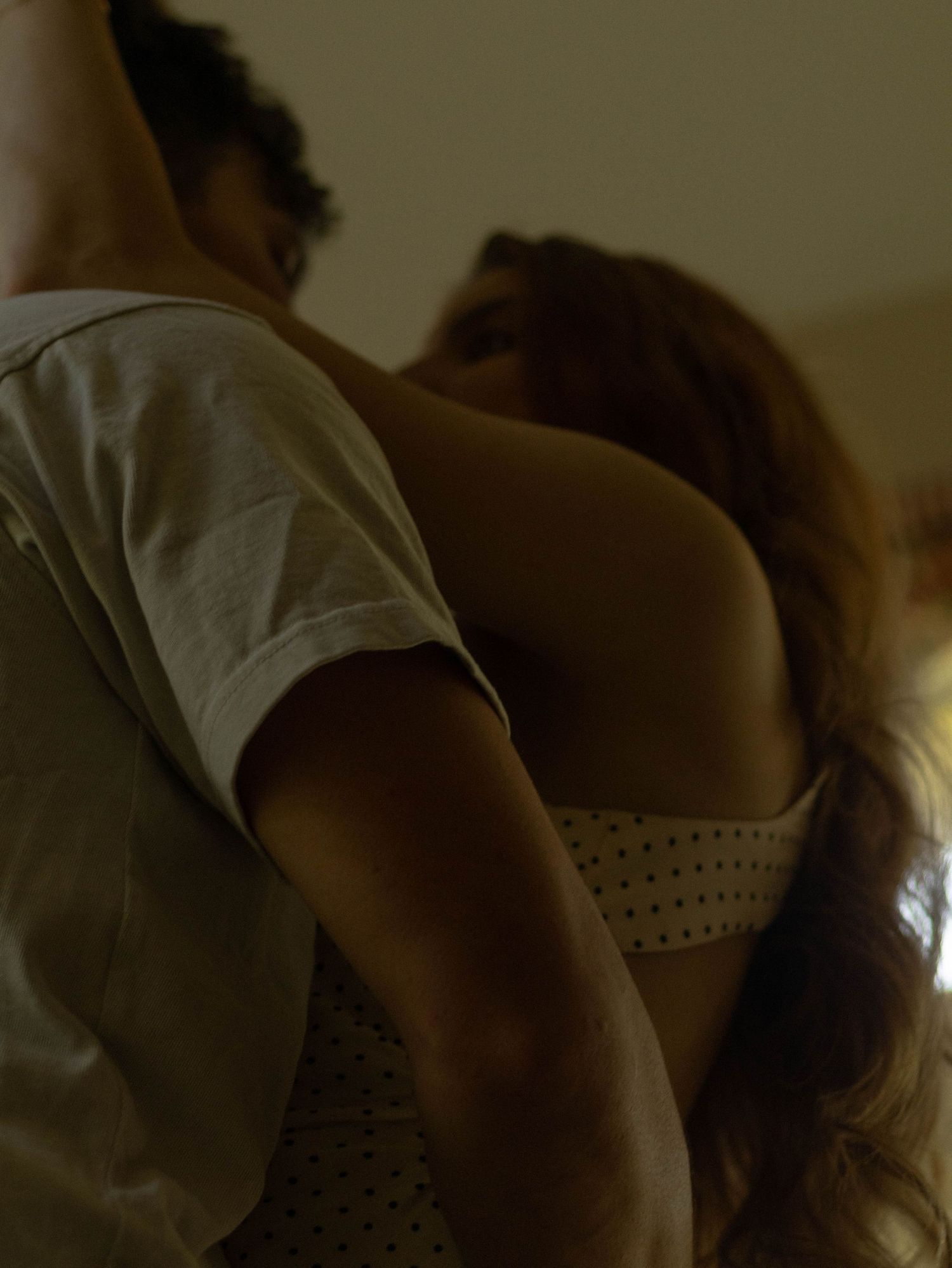 Two people embrace intimately in warm, dim lighting wearing casual white clothing.