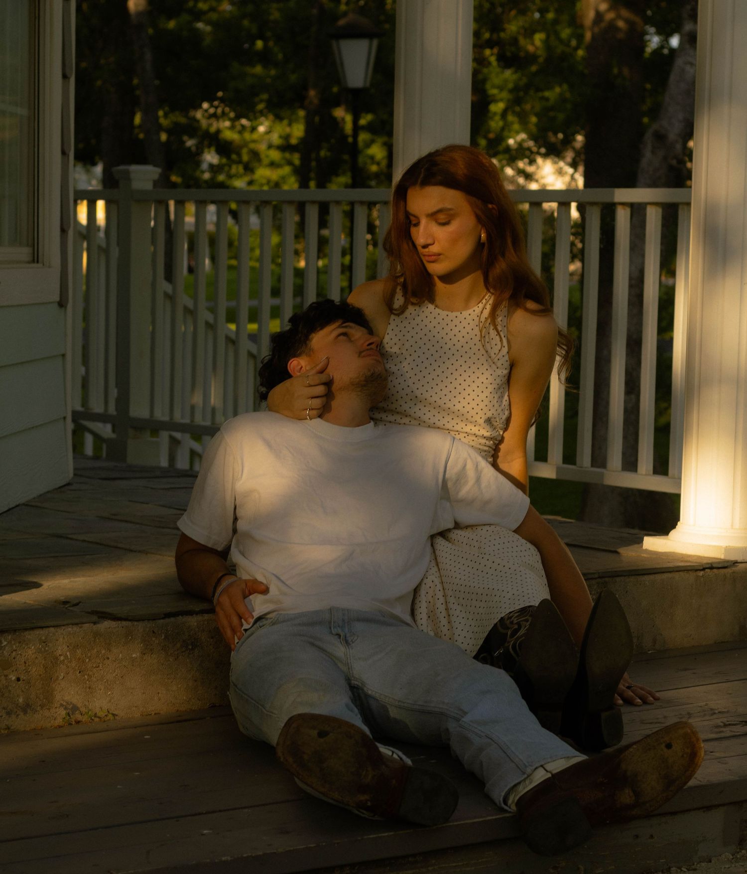Young couple sitting on porch steps at dusk, woman cradling mans head tenderly.