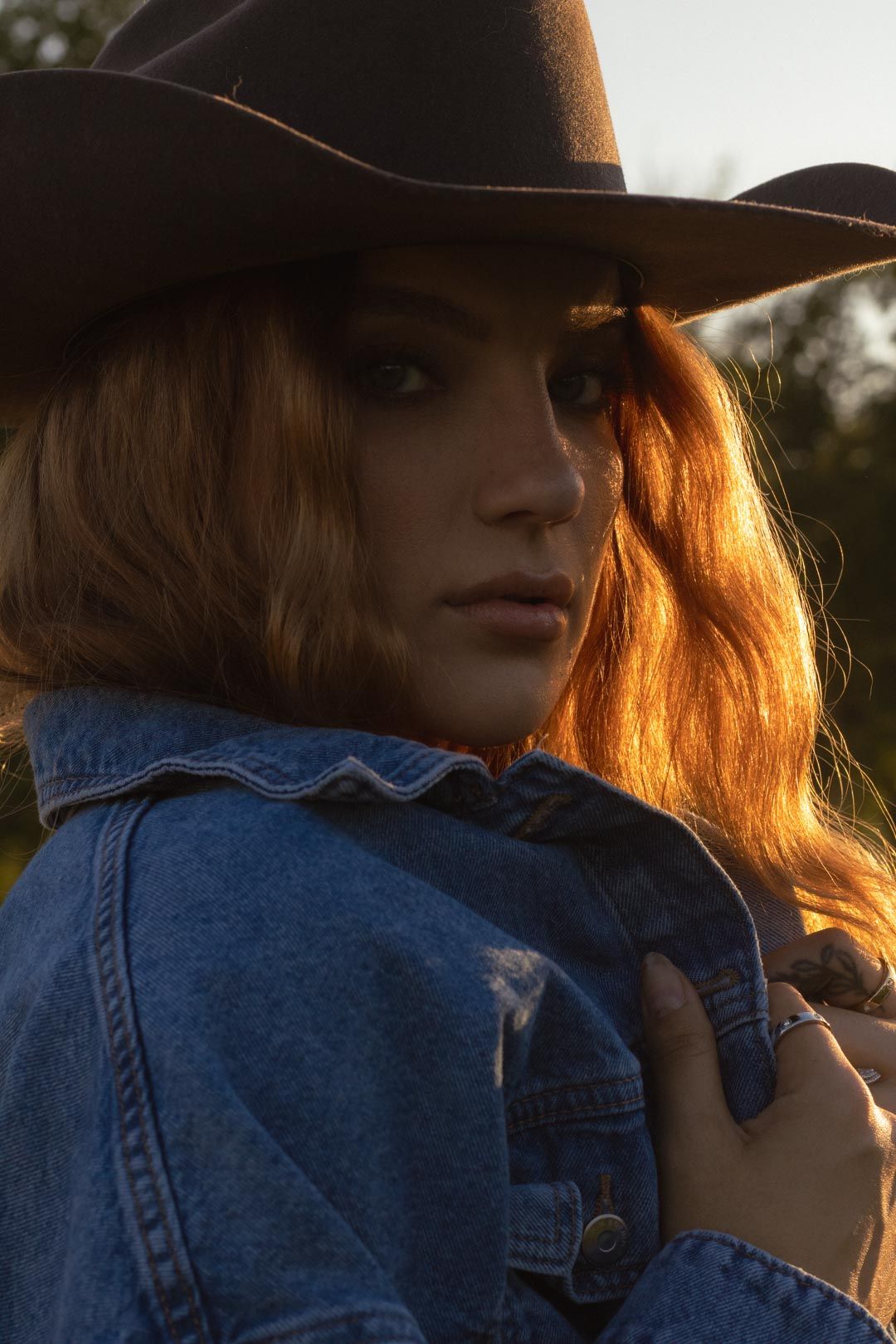 A person in denim and a brown hat photographed in warm sunset lighting.