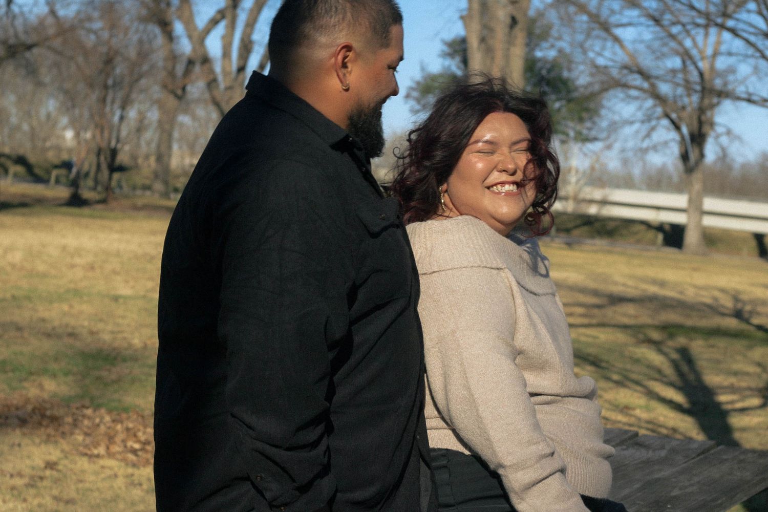 A candid outdoor shot of a couple sharing a laugh in winter clothing.