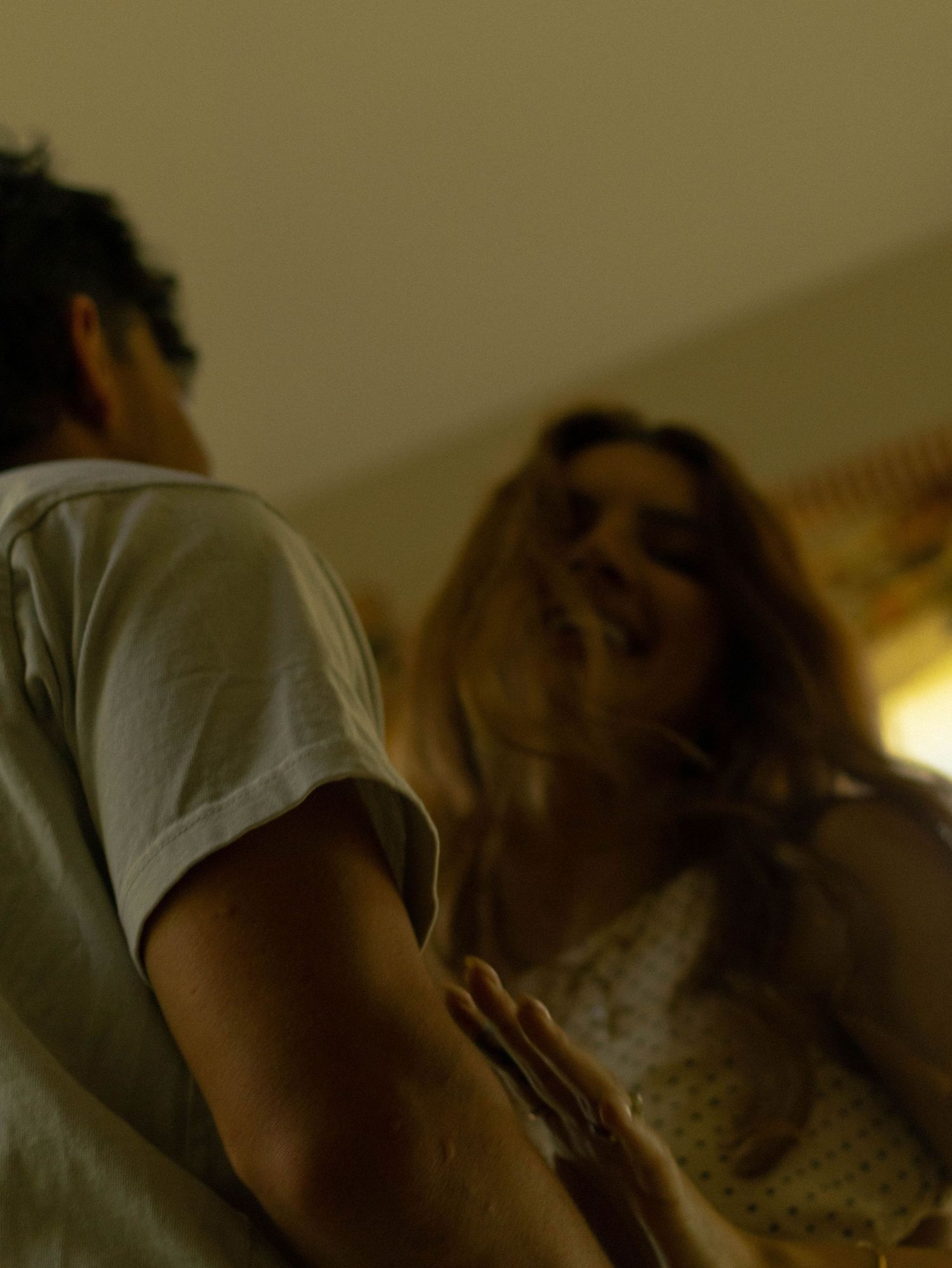 A man and woman share an intimate moment indoors, with warm ambient lighting creating a romantic atmosphere.