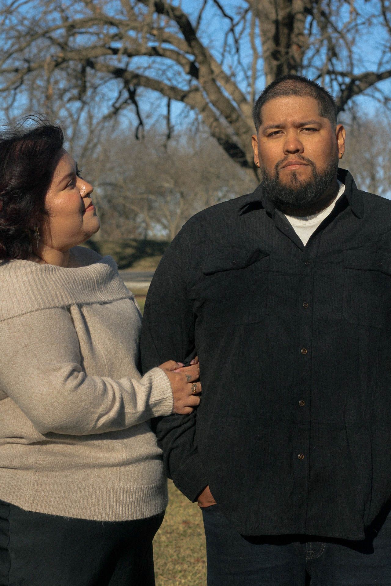 A couple poses together against a backdrop of bare winter trees.