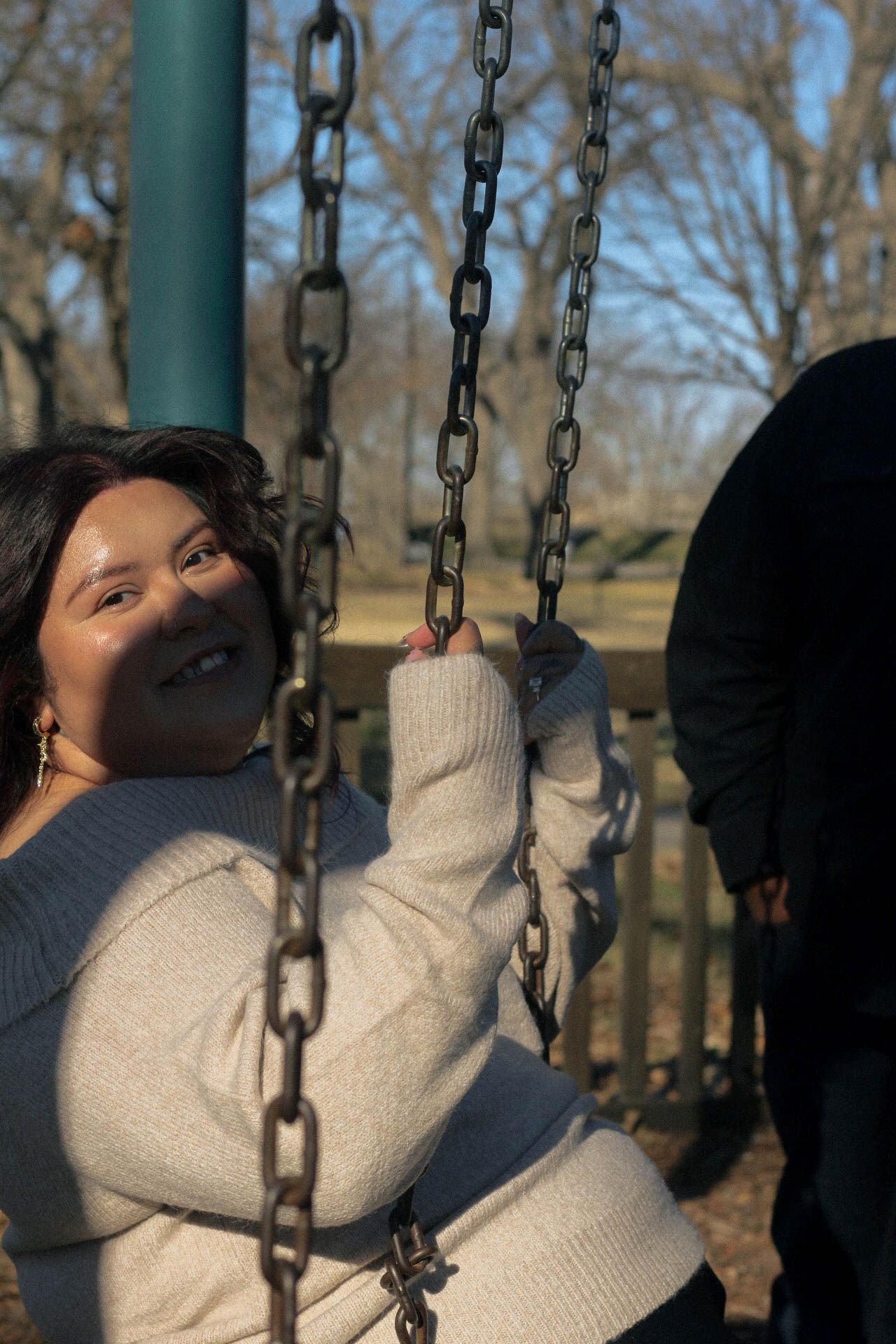 Person enjoying a playful moment on a swing set in a park on a sunny winter day.