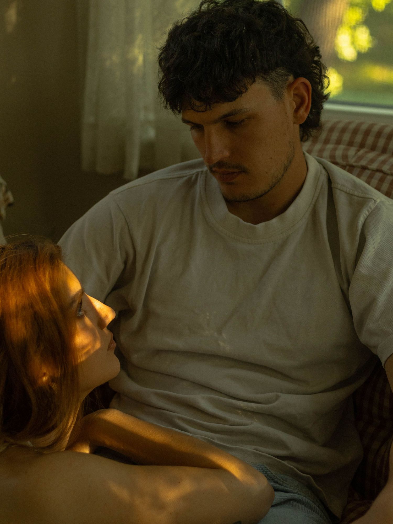 A young couple sharing an intimate moment indoors, bathed in warm golden light near a window.