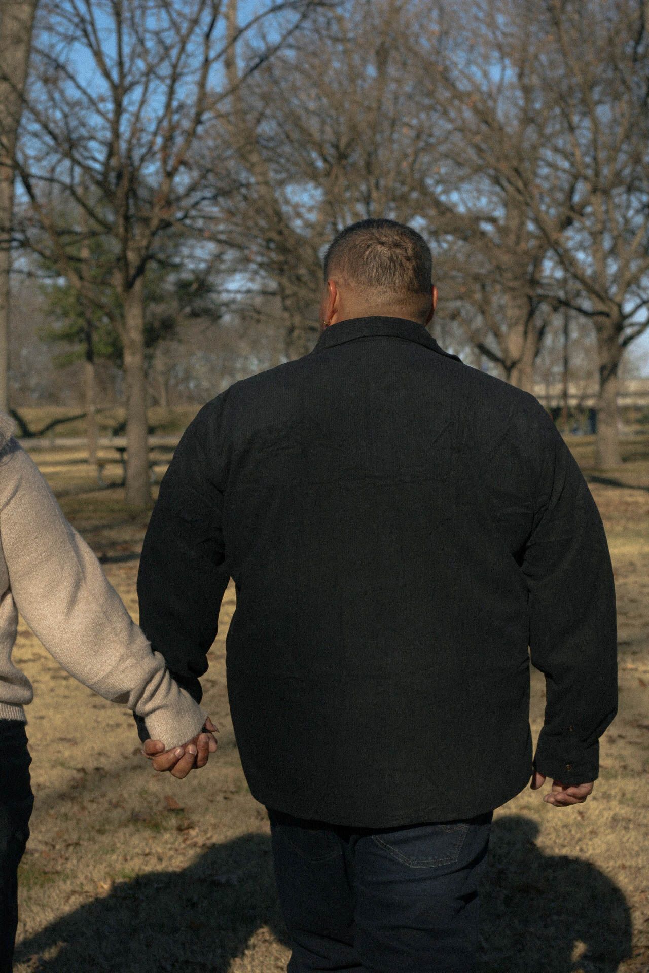 Two people walking together outdoors on a sunny day wearing contrasting black and beige outfits.