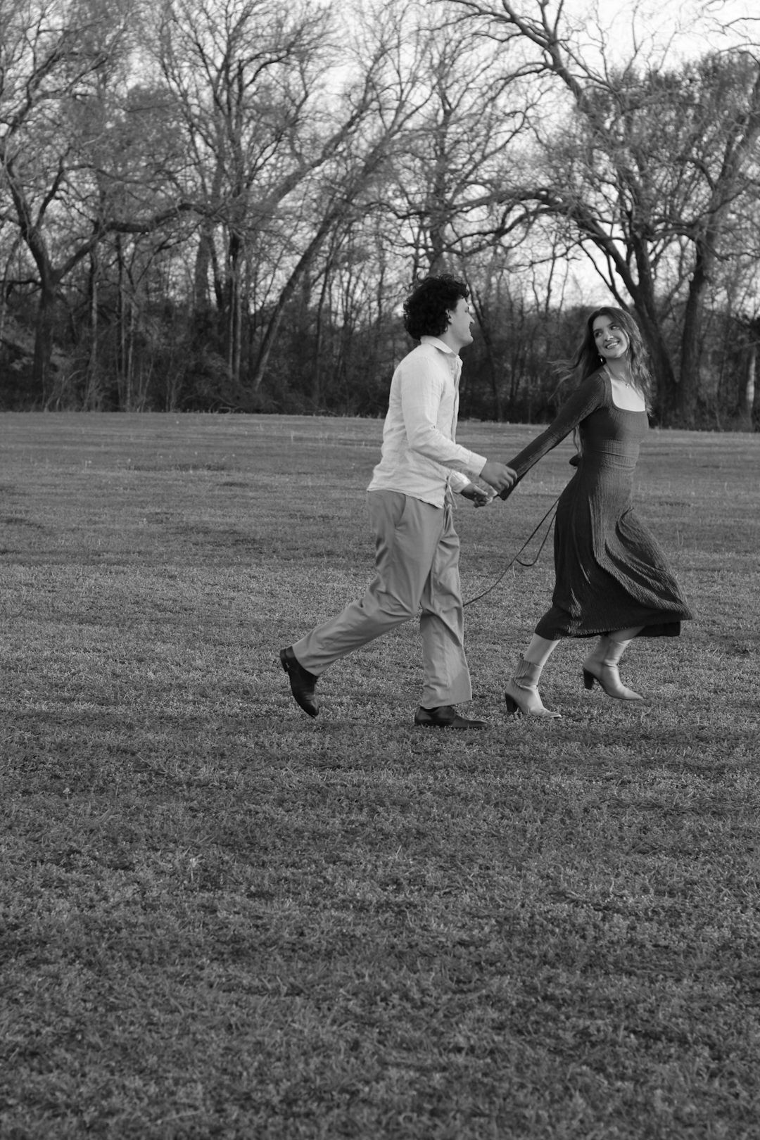 People walking and playing together in a grassy field with bare trees in background.