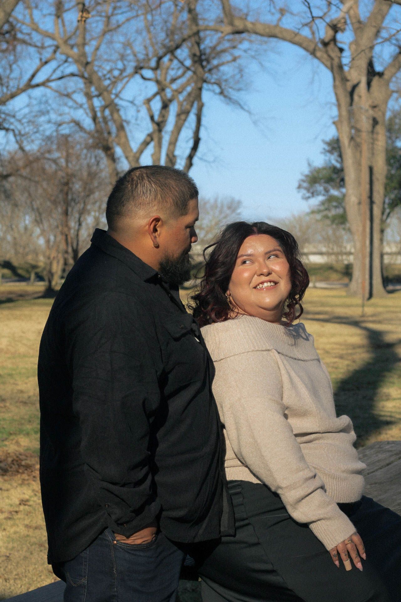 Two people share a romantic moment outdoors against a backdrop of bare winter trees.