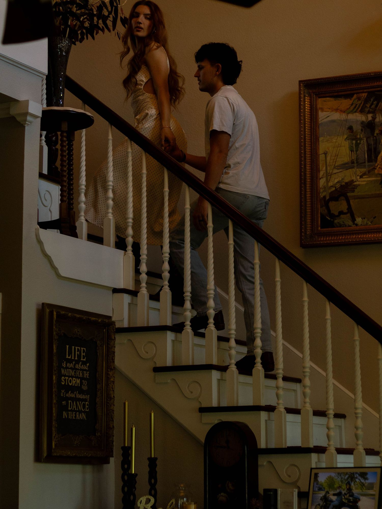 A man and woman share an intimate moment on a grand staircase inside an elegant home.
