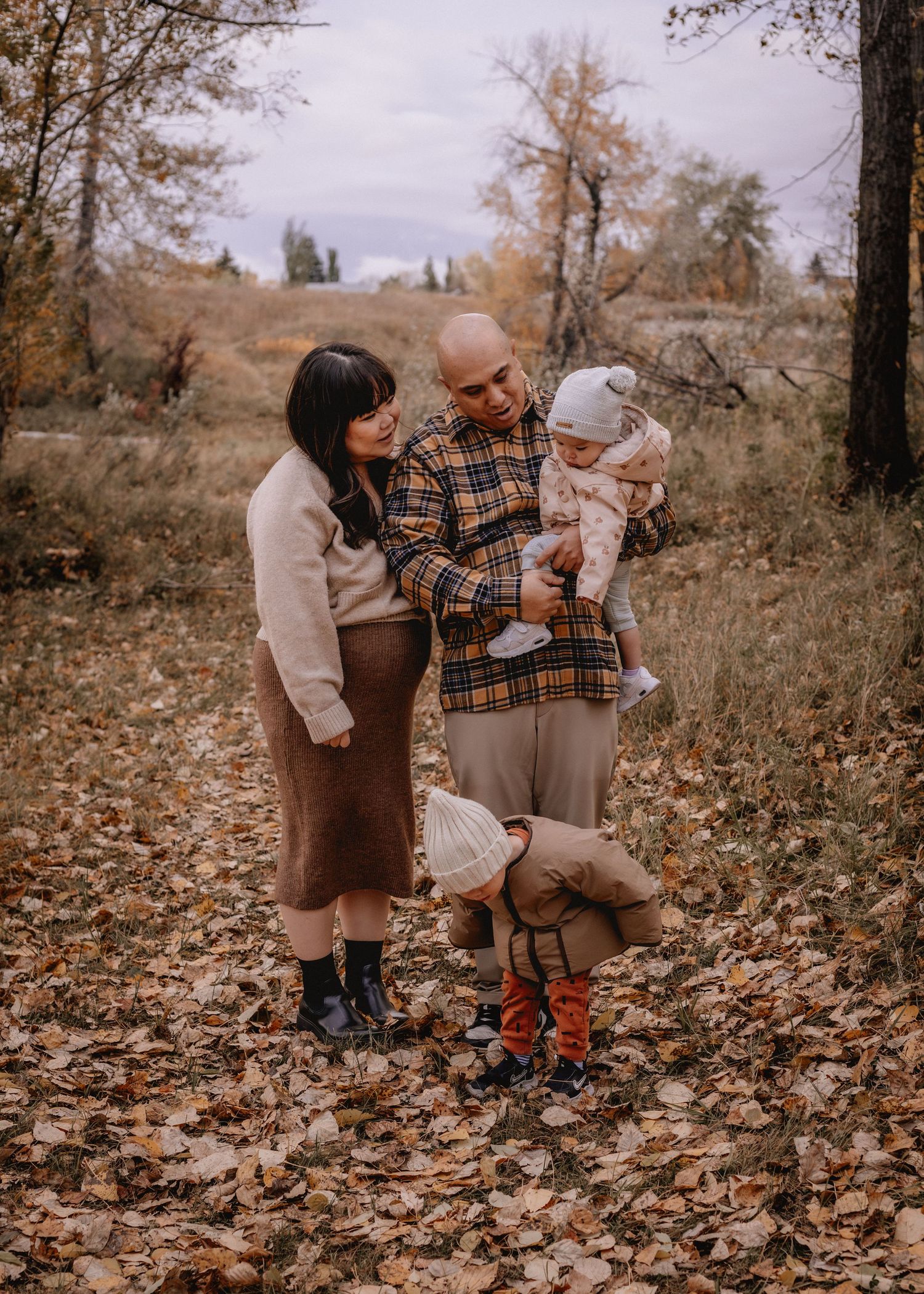 Family playing together in fallen autumn leaves on the ground in Carburn Park, AB during family photoshoot