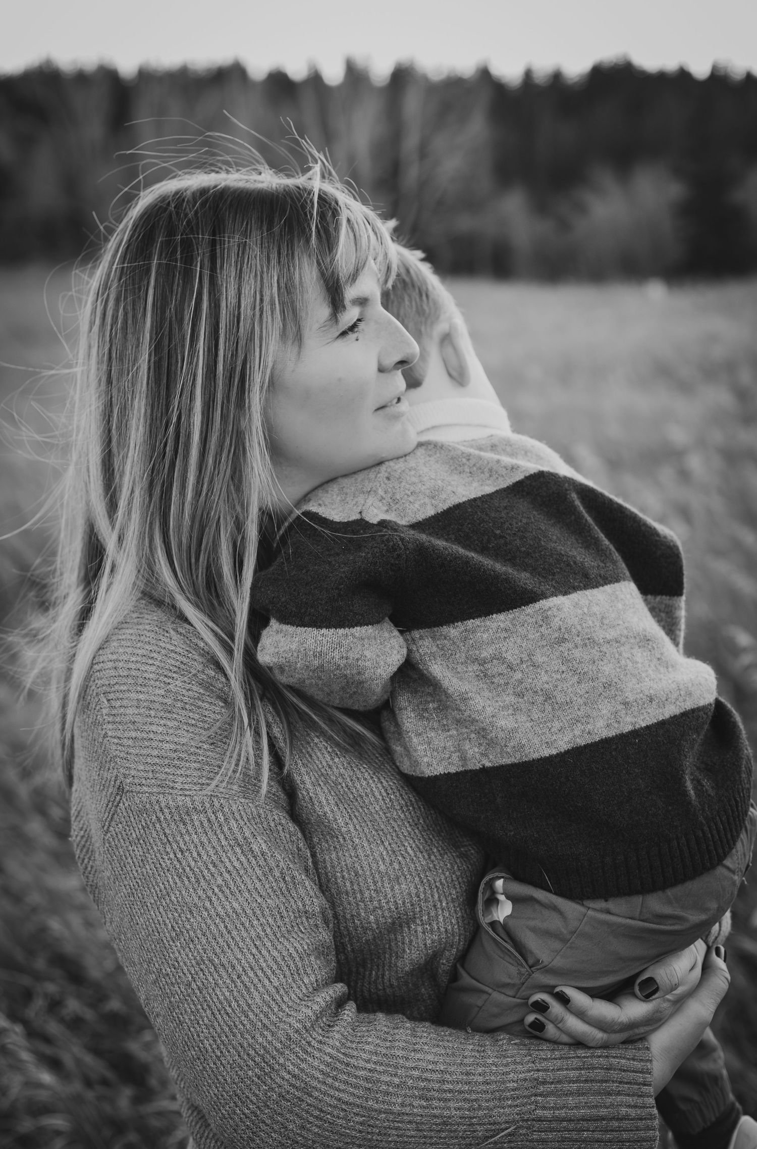 Black and white photo of a woman holding a child in a striped sweater in an outdoor field In Fish Creek Park.