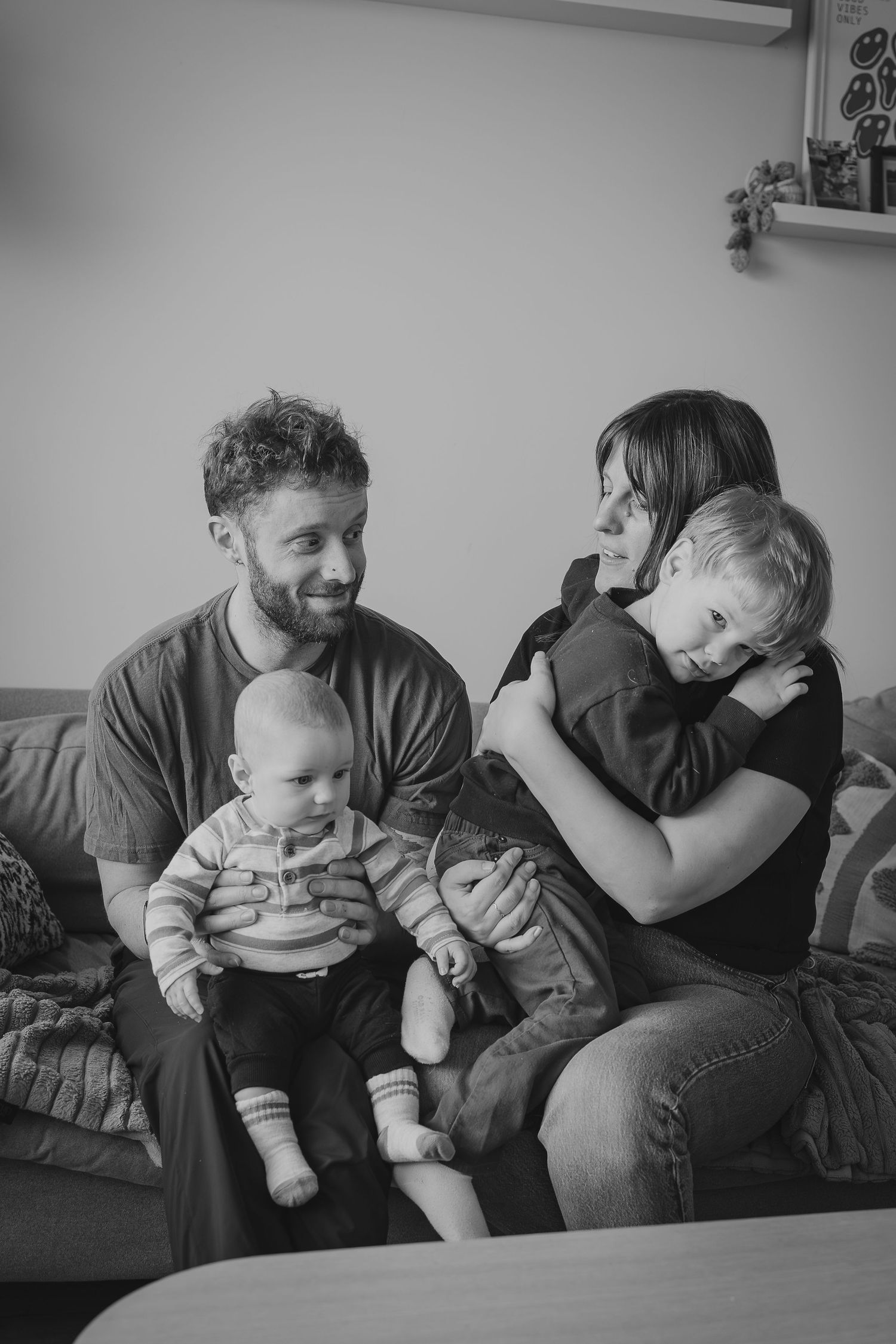 Black and white family portrait of parents with two young children sitting together on a couch during in-home Calgary photography session