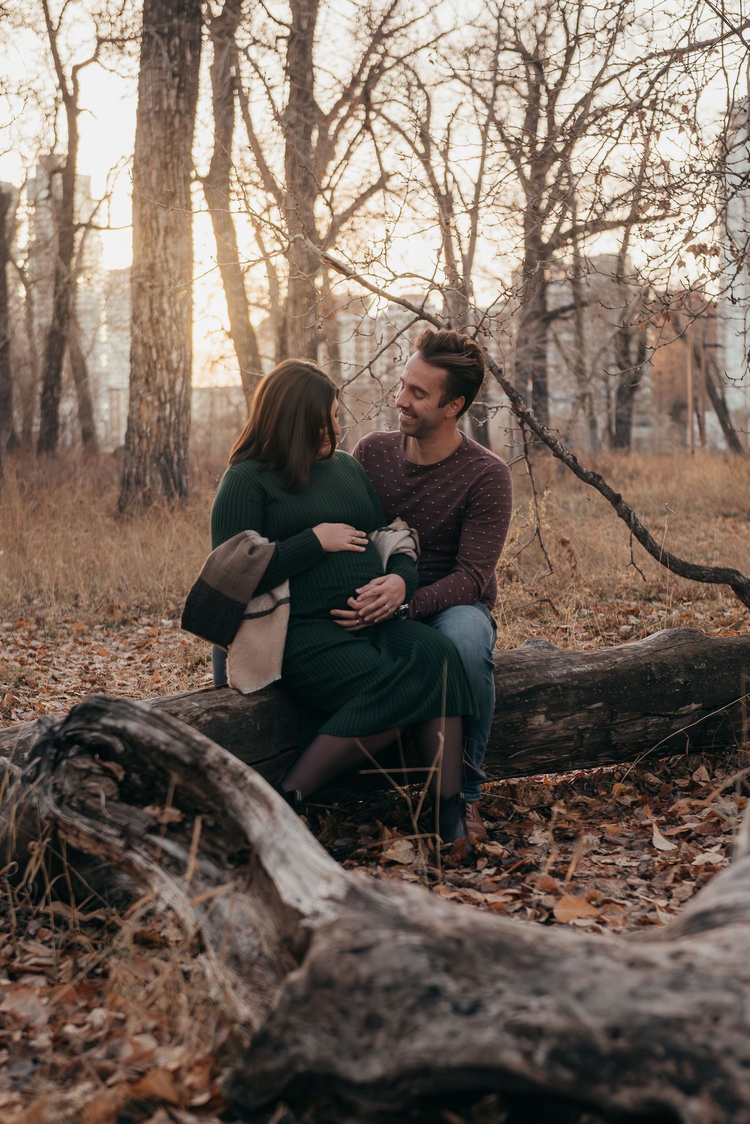 Calgary couple sitting on fallen log during autumn maternity photoshoot in wooded area.