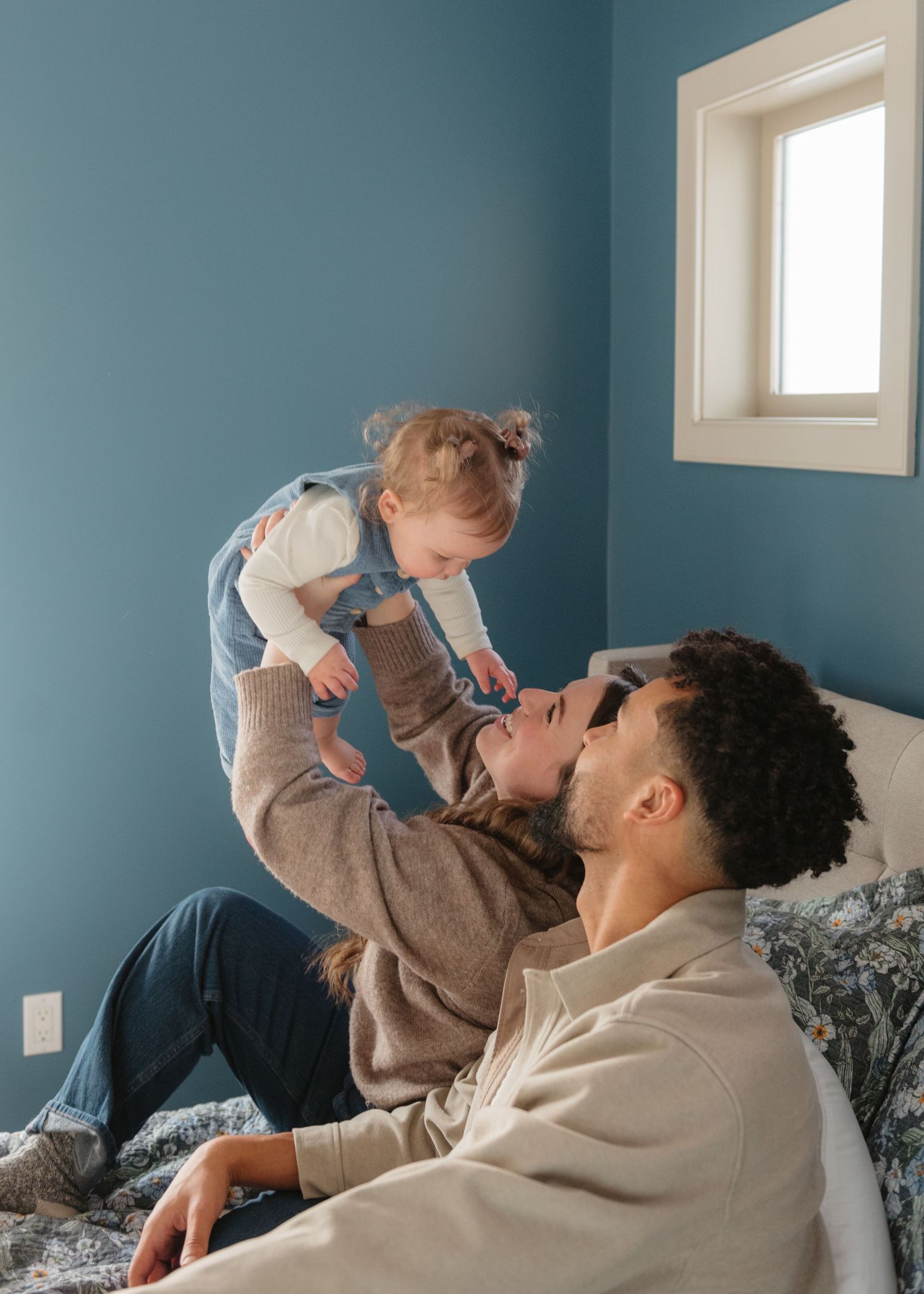 Calgary parents and baby share playful moments on a bed with blue walls in the background.