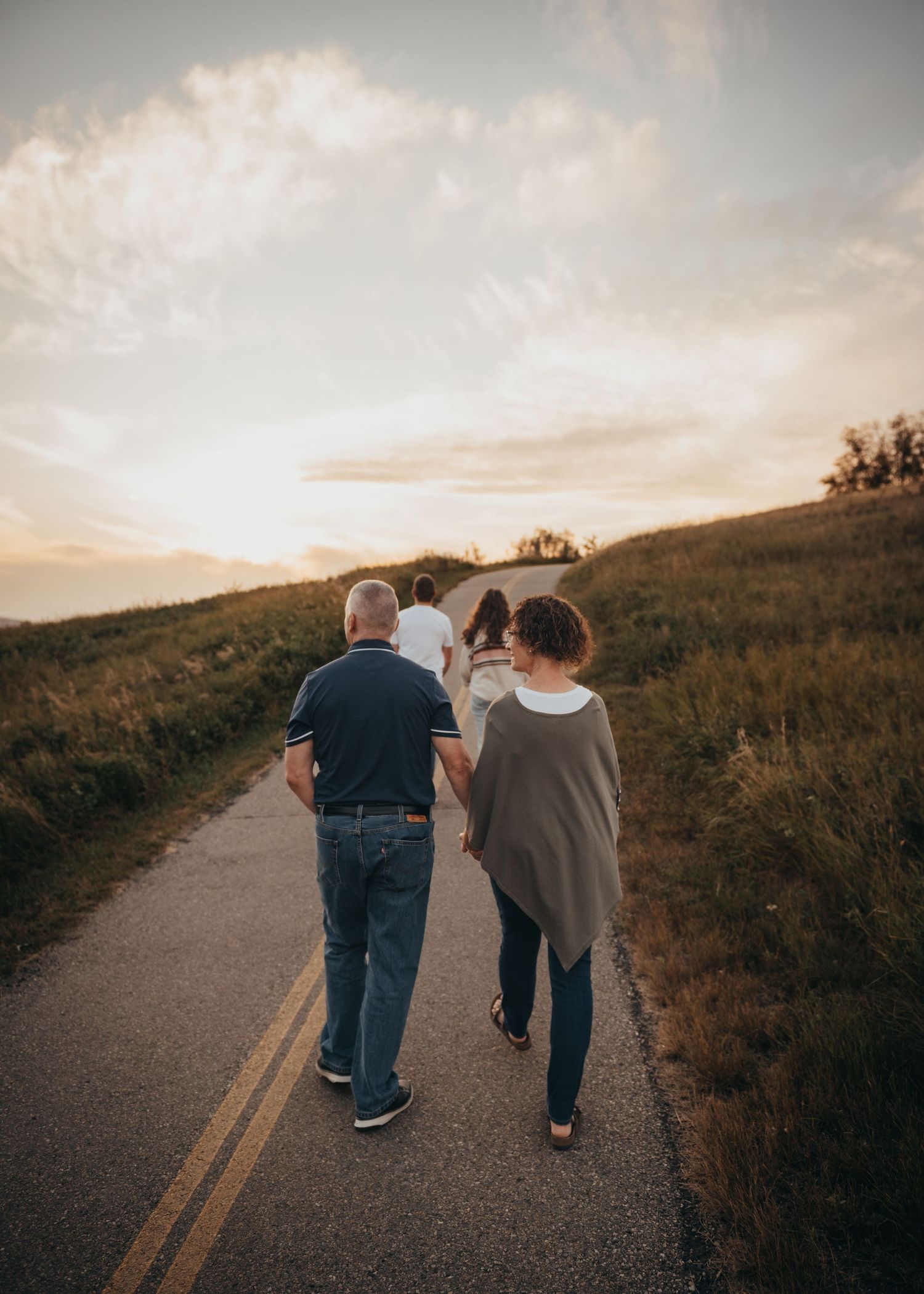 Family walking together down a winding Calgary path at sunset, surrounded by green hills and a glowing sky.