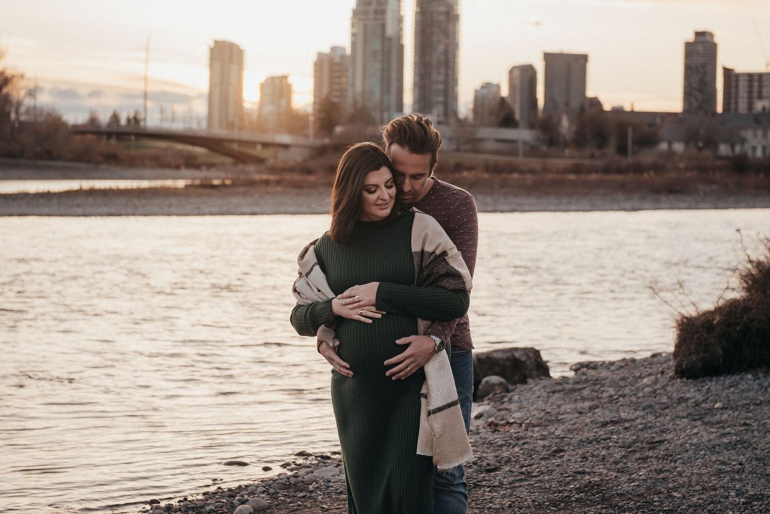 Maternity photoshoot by the Bow River with Calgary's city skyline at golden hour.
