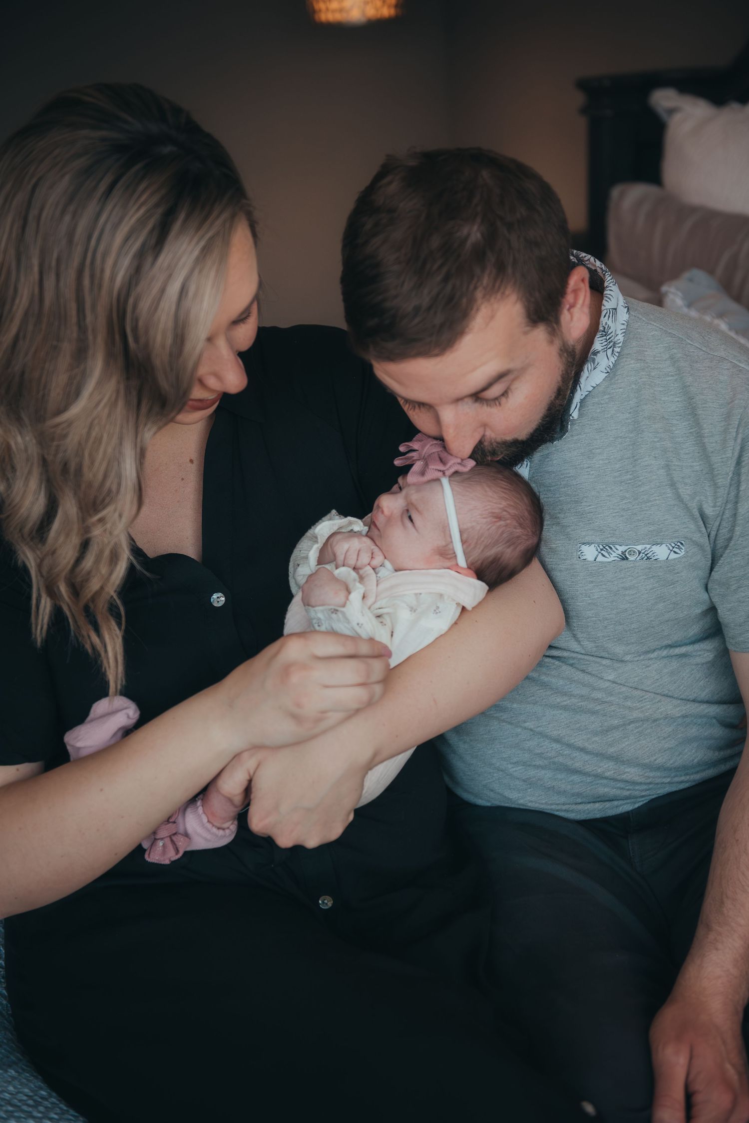 Parents sharing gentle kisses with their newborn baby during an indoor photo session.