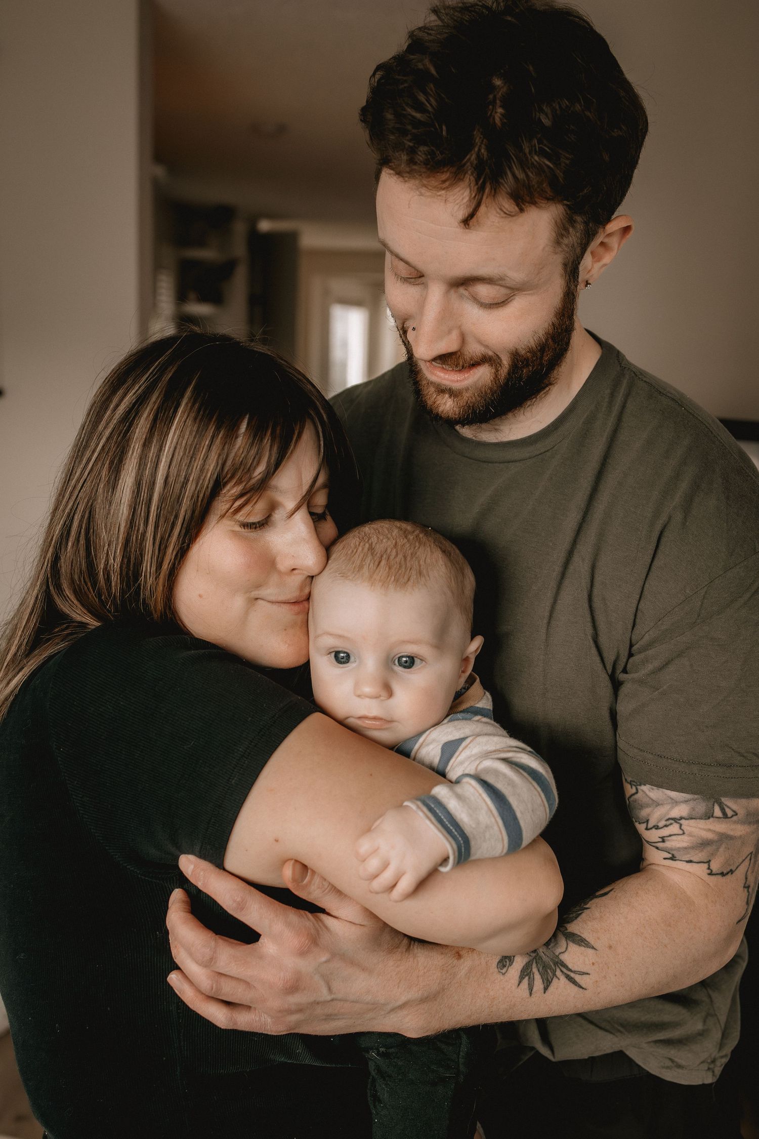 A young couple smiling and cuddling their alert baby boy in their Calgary, AB home in a warm, intimate family portrait.