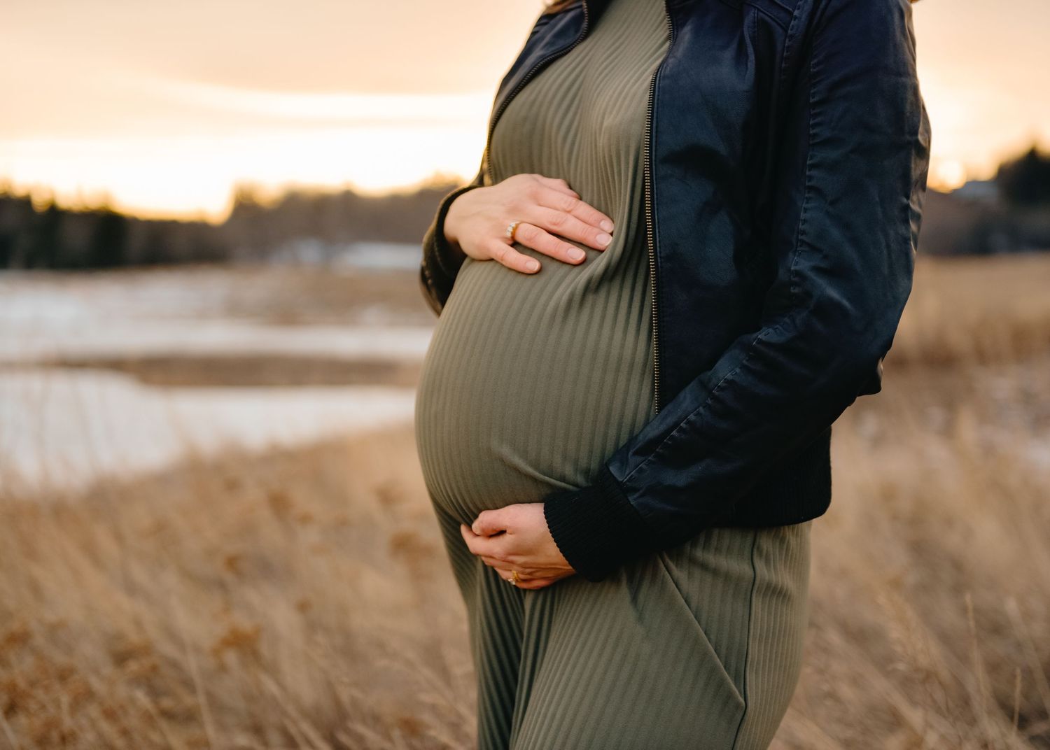 Maternity photoshoot in a golden Calgary field during sunset. Mom holding her baby bump close-up.