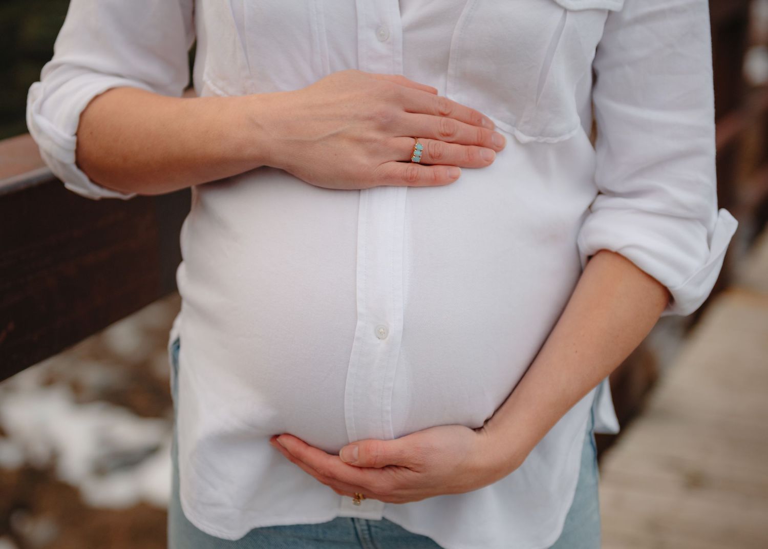 Close-up of hands gently cradling a pregnant belly in white button-down shirt.