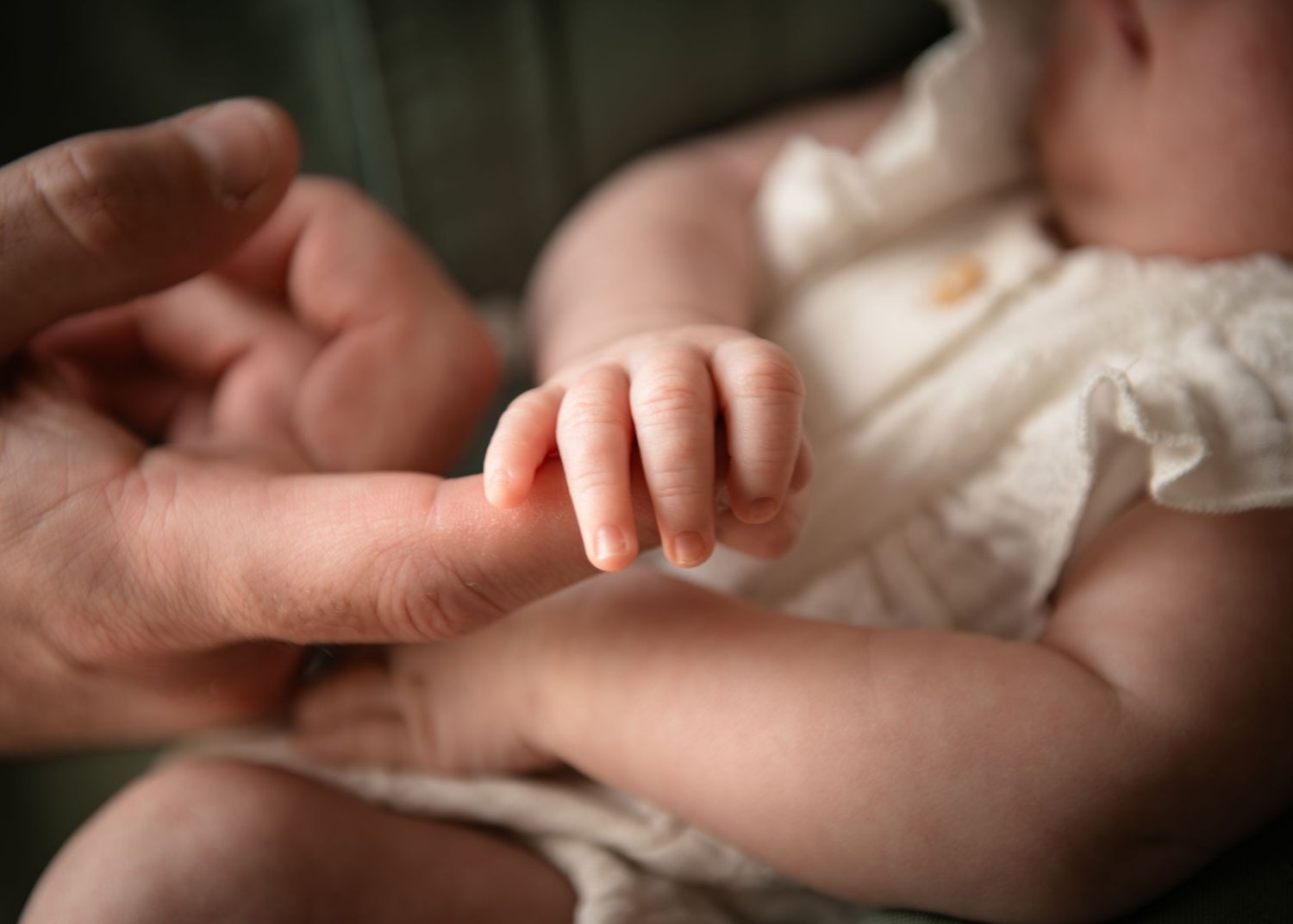 Newborn baby grasping dads finger, close-up of tiny infant hand holding parent finger in tender moment during lifestyle photoshoot