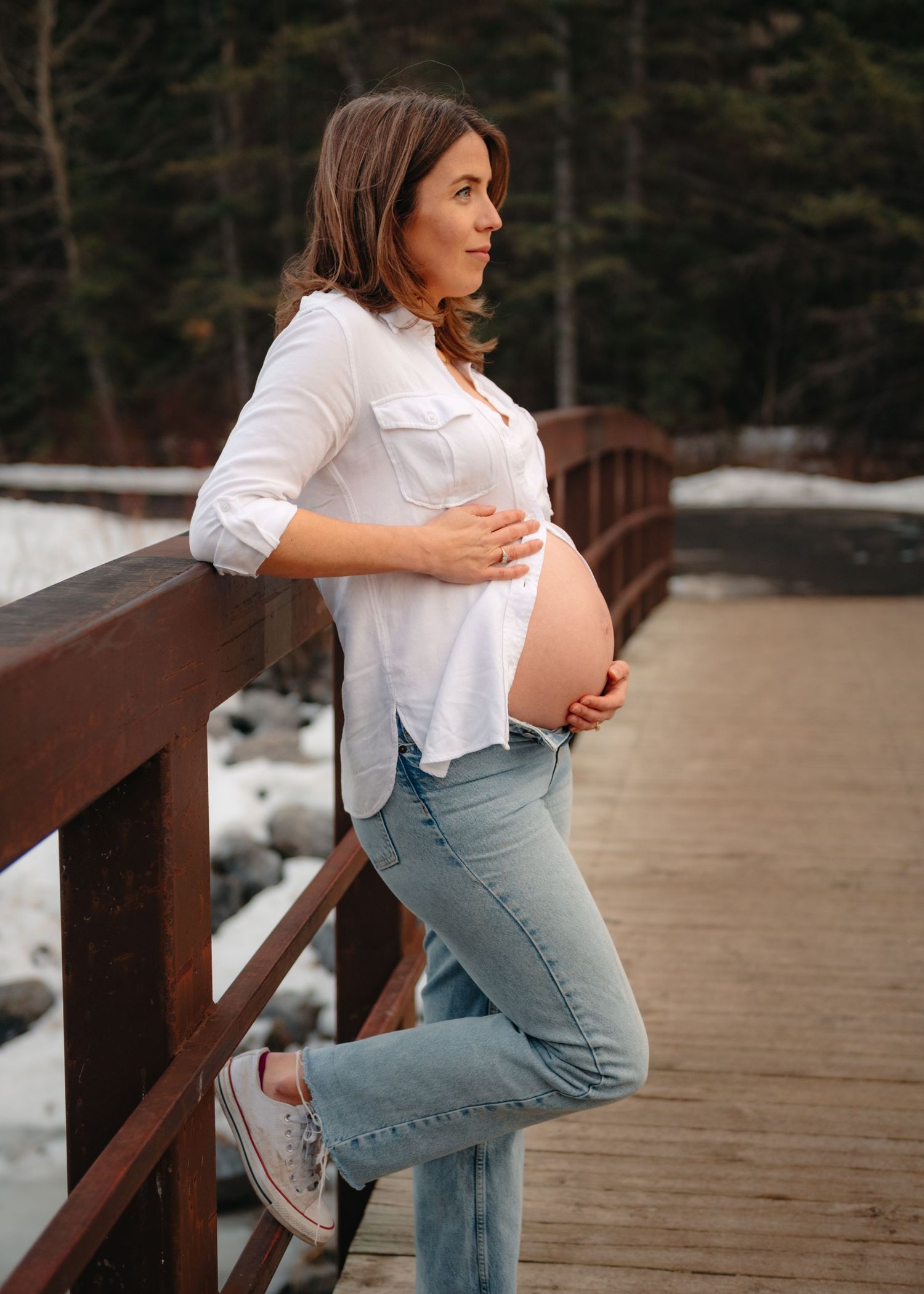 Side view maternity portraits on wooden bridge during winter showing baby bump.