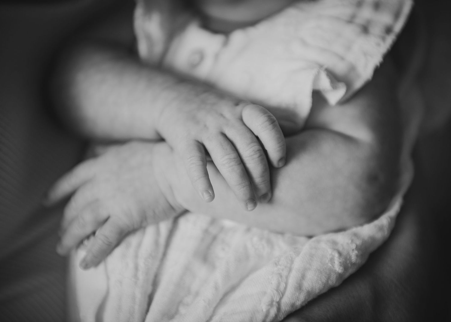 Black and white close-up photo of a newborn baby's tiny delicate hands resting peacefully.