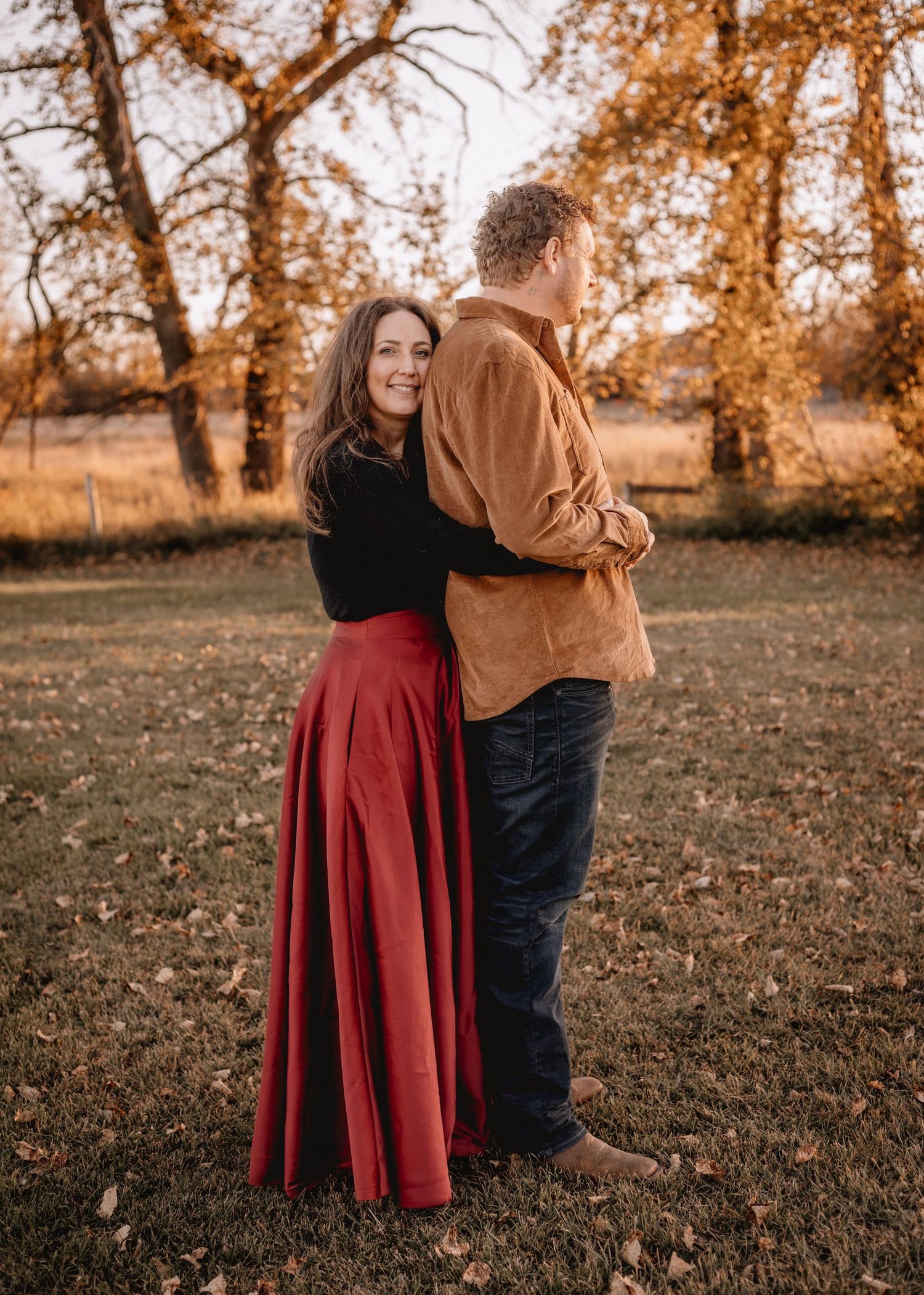 A couple embraces in a High River, AB autumn field with golden sunlight filtering through trees.