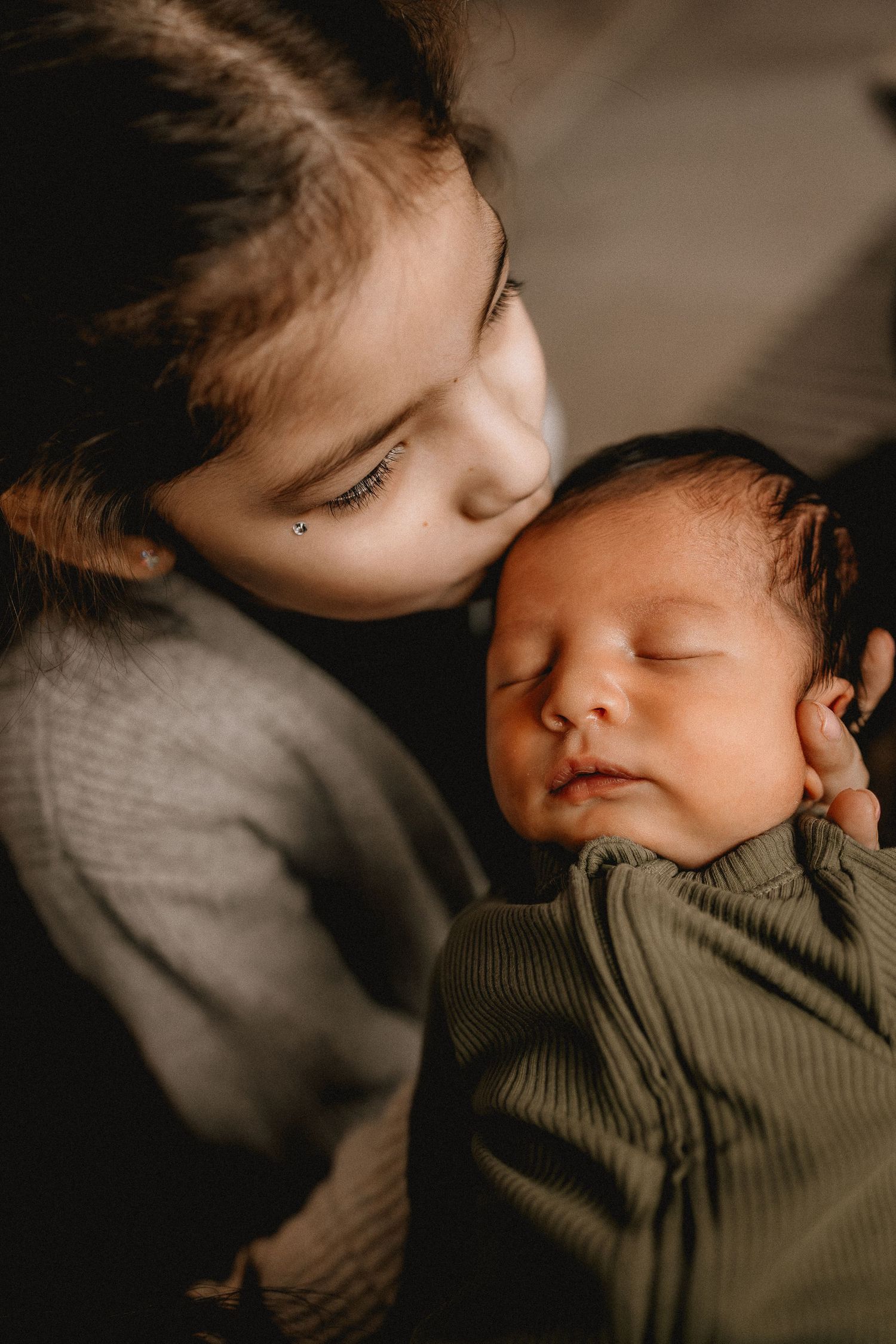 A tender moment captured between siblings as older child gently kisses sleeping baby in green outfit during newborn photography session
