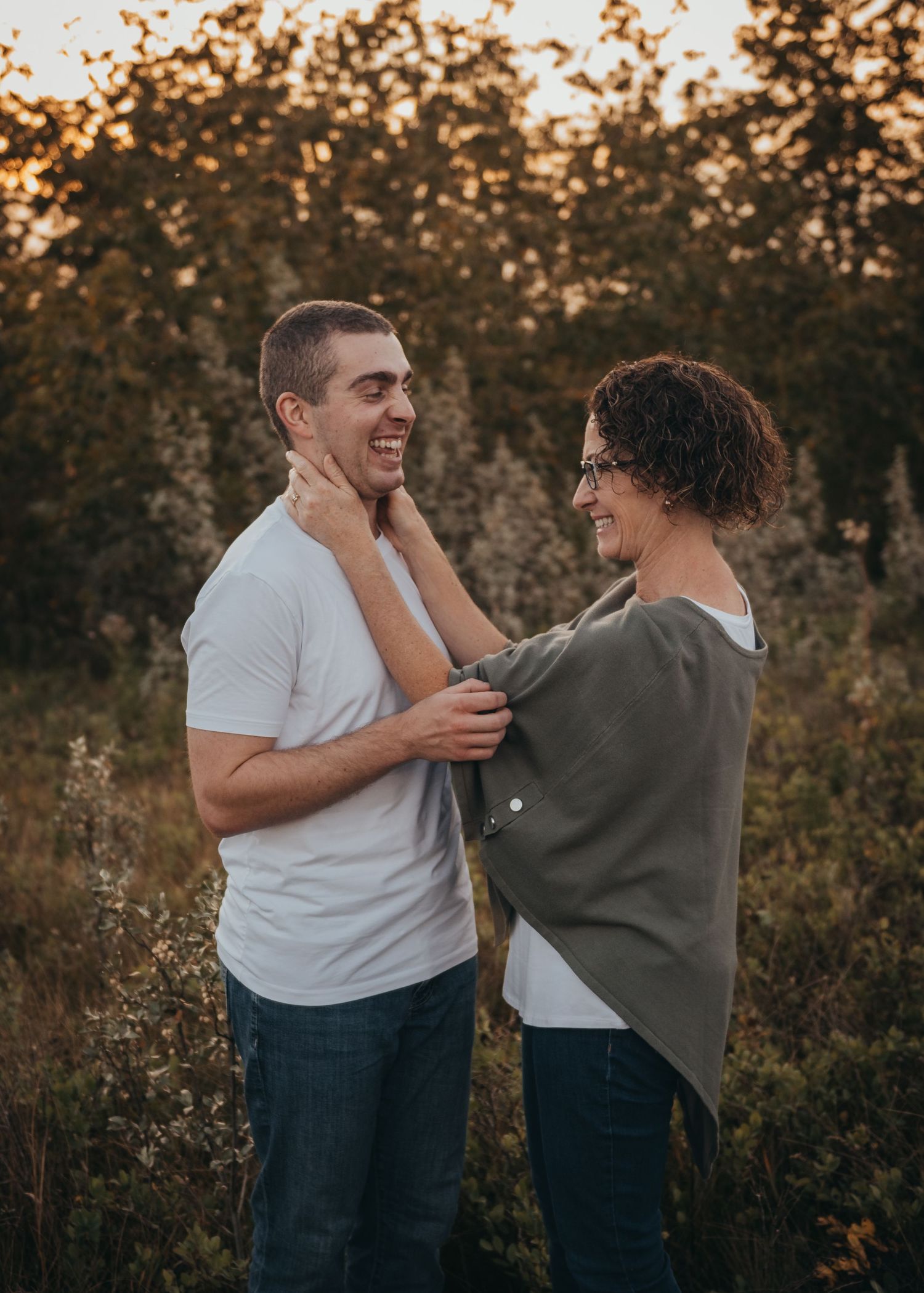 Mother and son smiling and laughing together in a golden hour outdoor setting, woman touching sons face affectionately.
