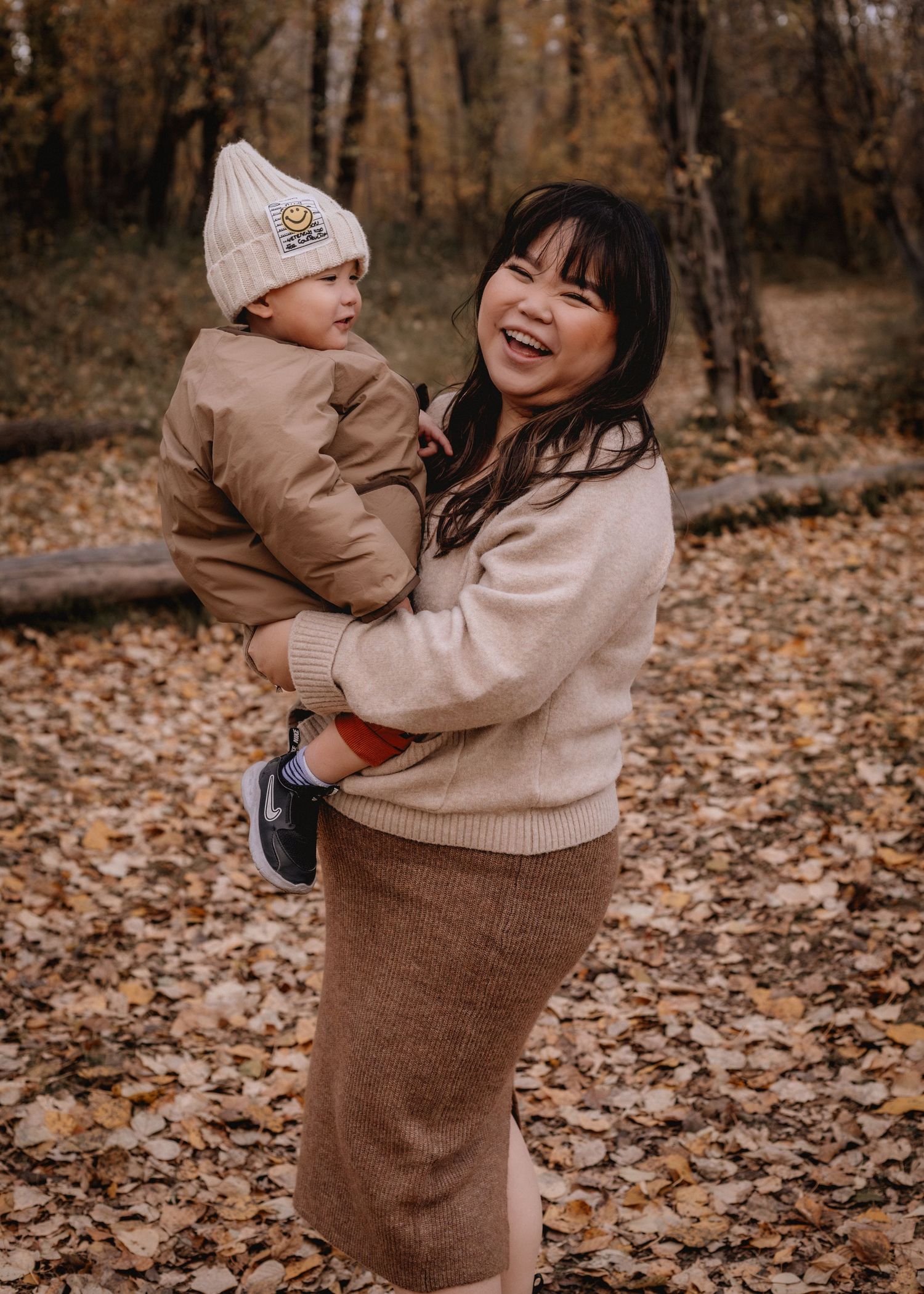 Parent and child playing together on autumn leaves in matching beige outfits.