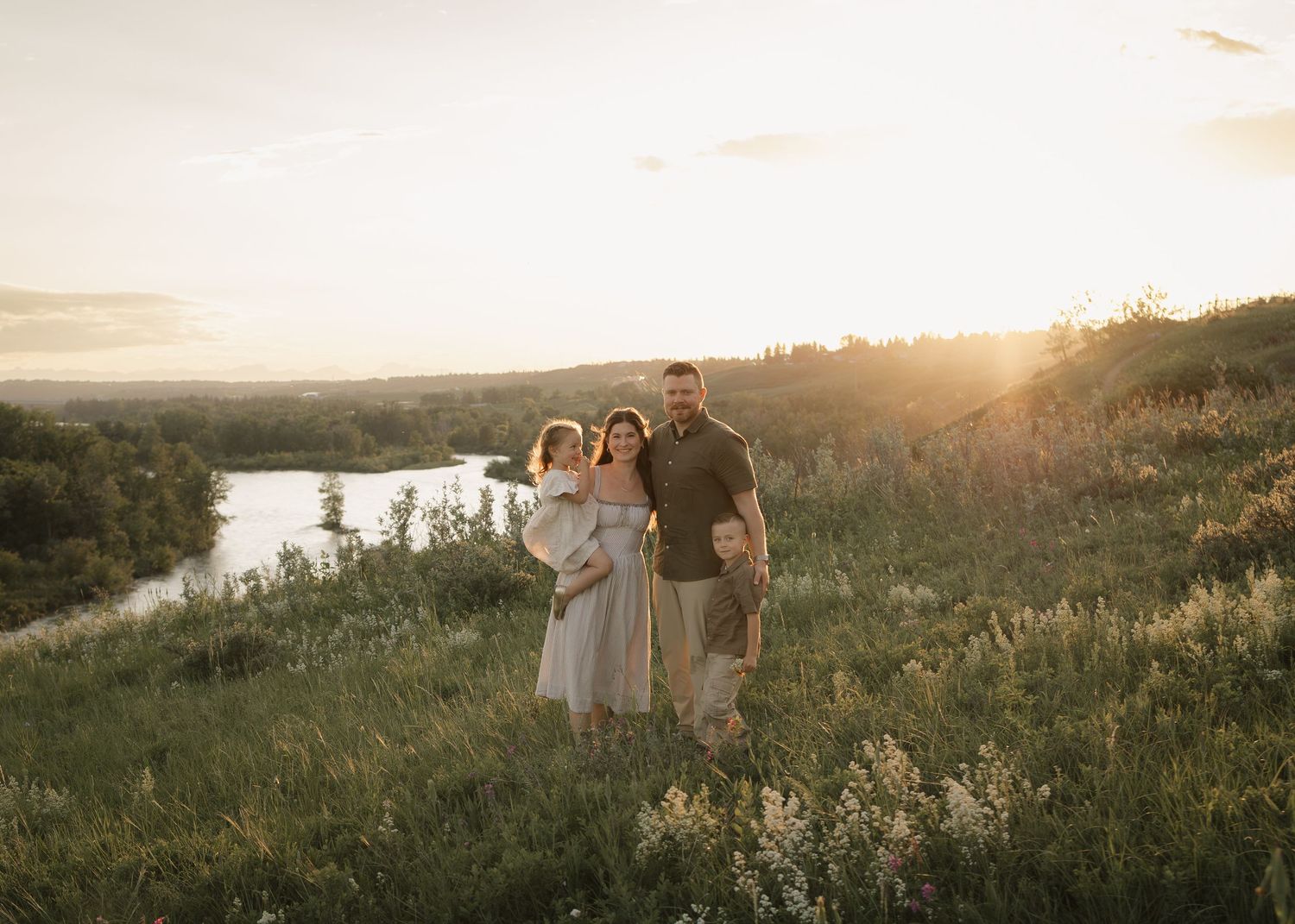Family of four during golden hour standing on a ride over looking the river valley for photos