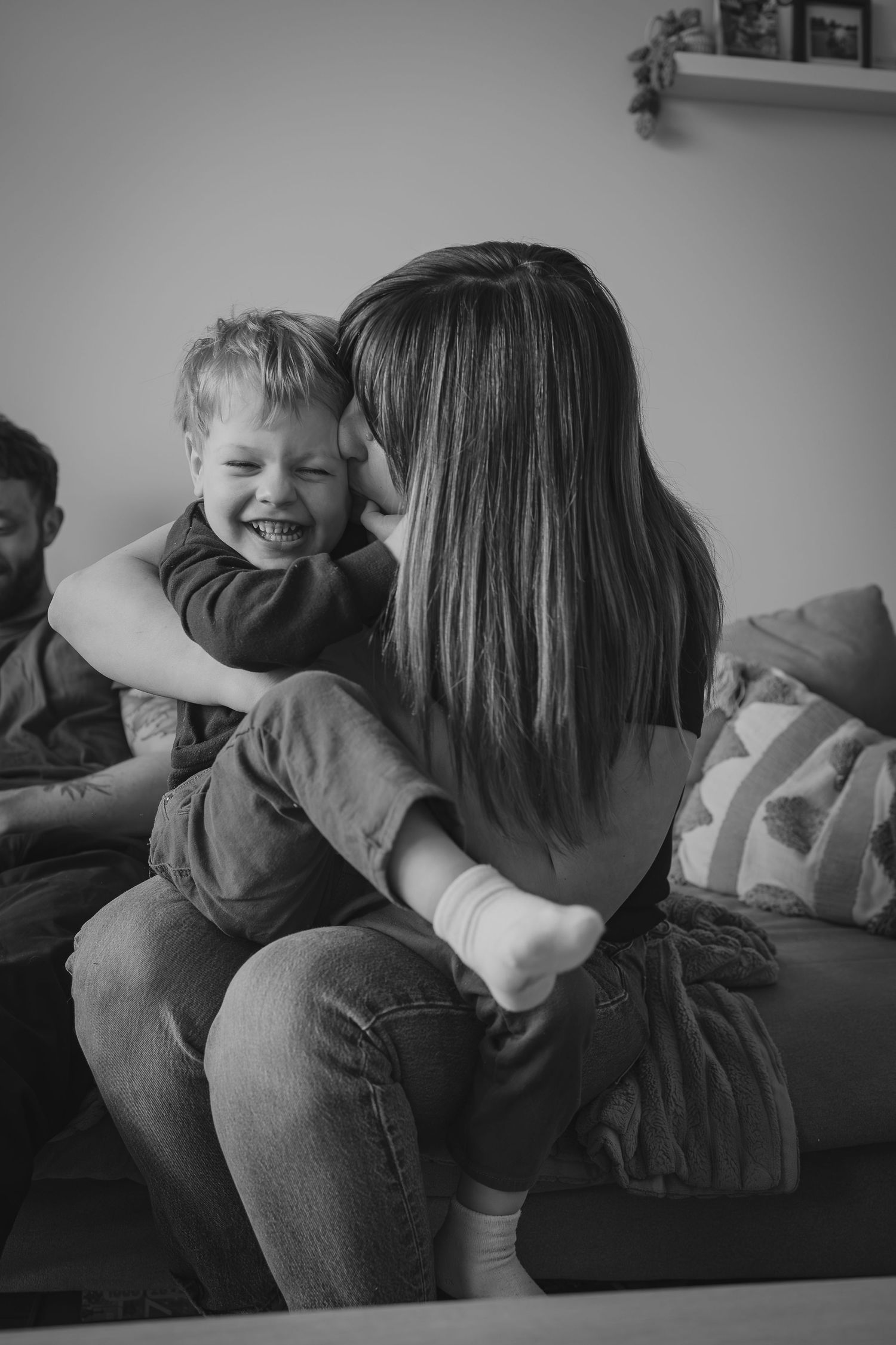 Black and white photo of a mother hugging and kissing her laughing young son on a couch at home lifestyle Calgary, AB photographer session