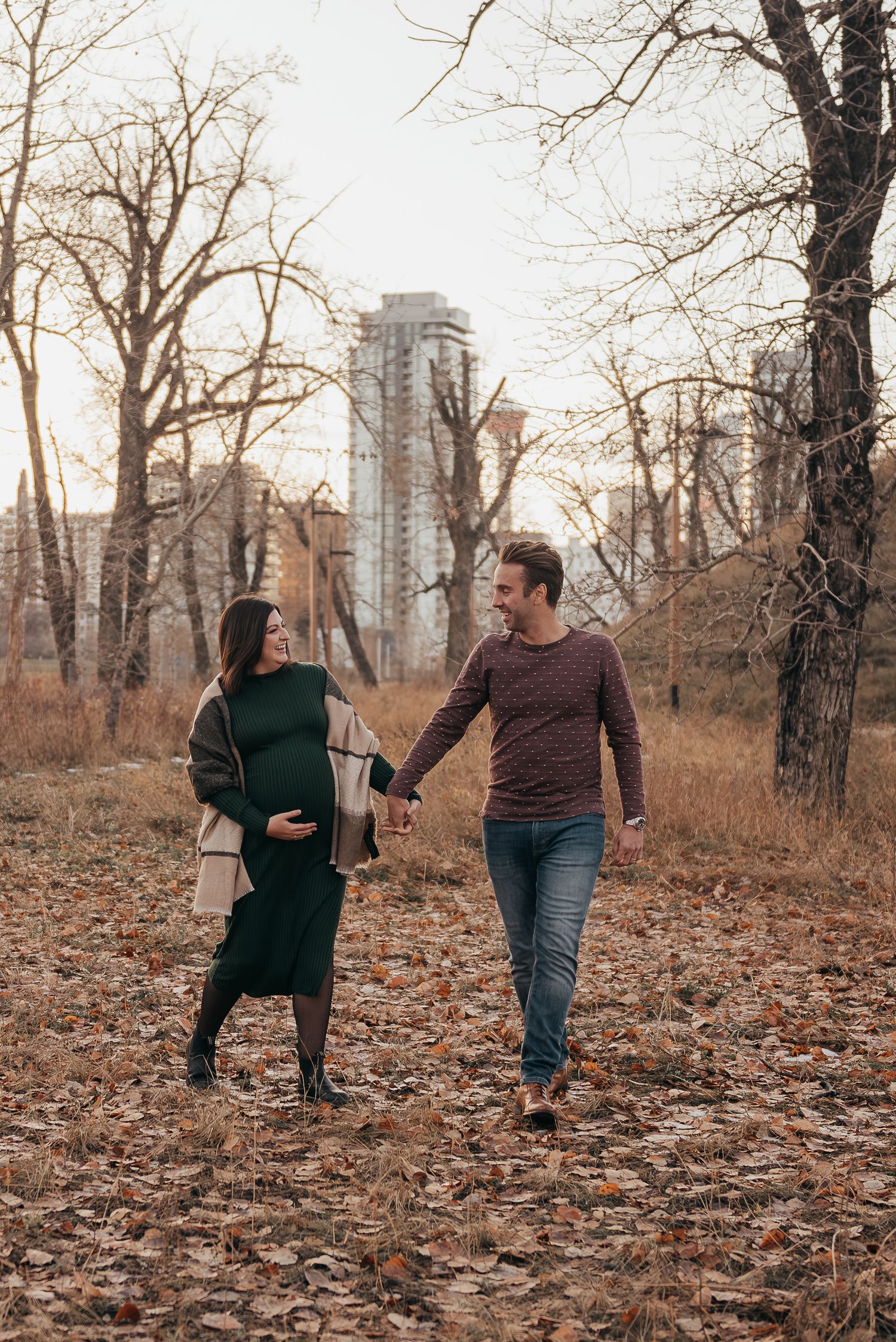 A Calgary couple walks through fallen autumn leaves with city buildings visible in background.