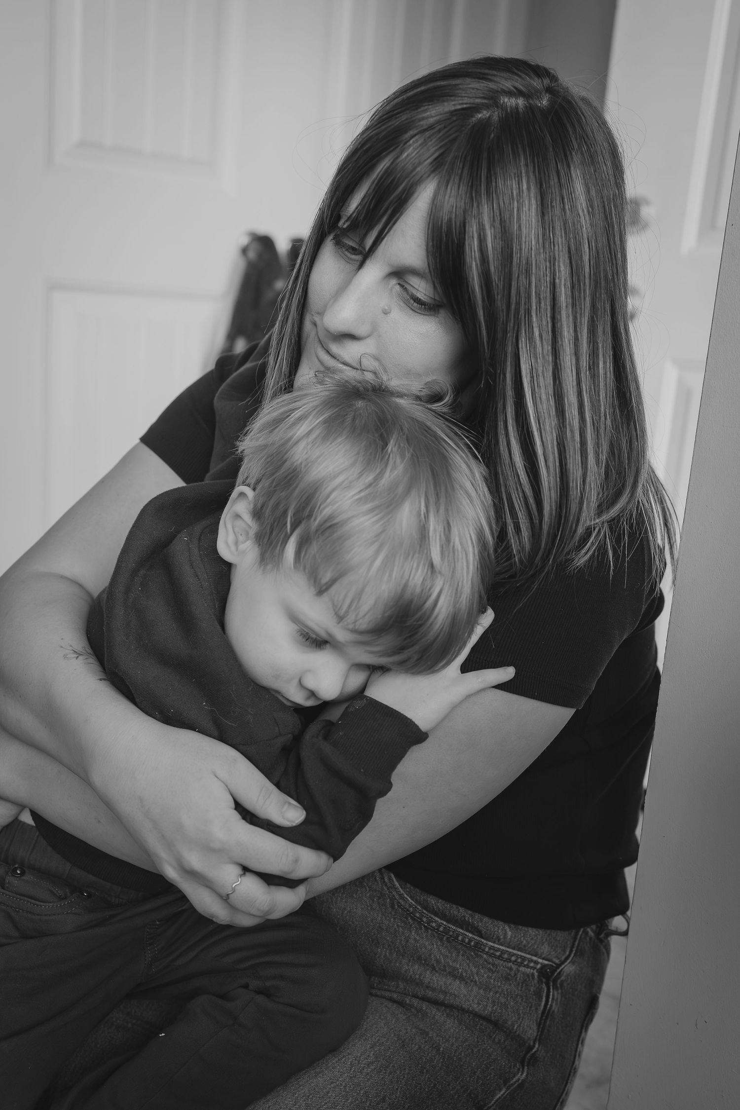 Black and white photo of a mother tenderly embracing her young toddler son indoors during Calgary family photographer session